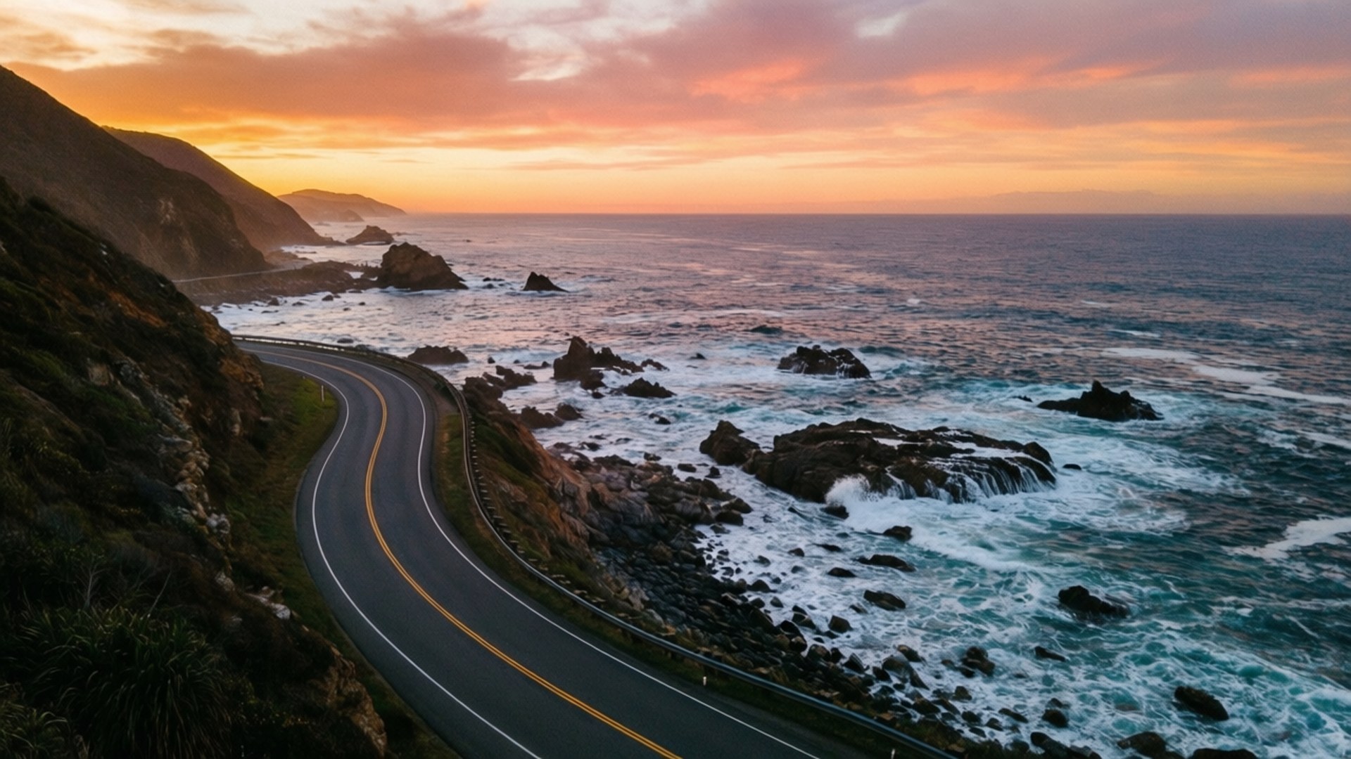 Coastal Drive 壁紙 — 蜿蜒的海岸公路沿著崎嶇的懸崖蜿蜒而行，波濤拍打岩石，天空燃燒著夕陽。