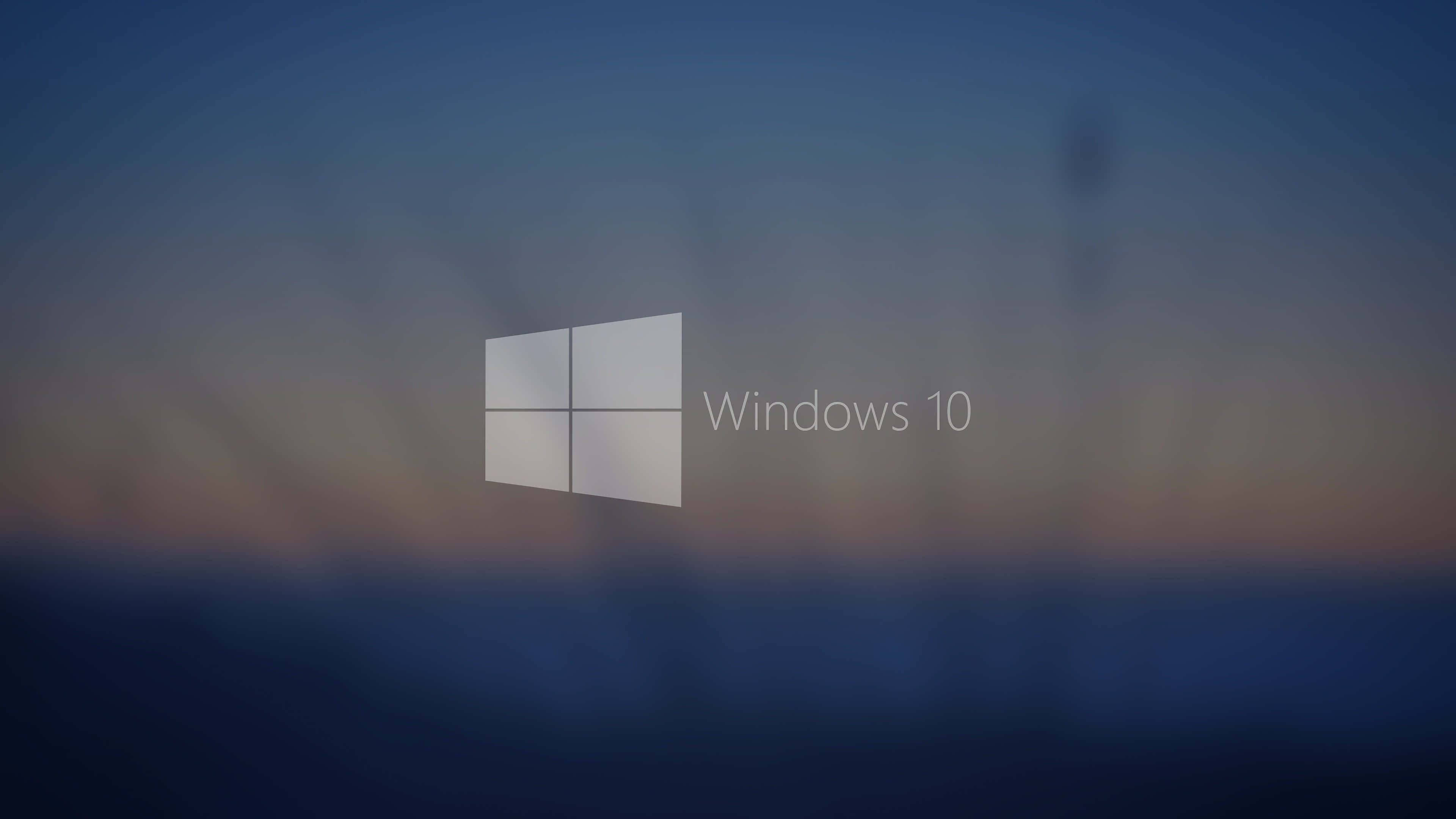 Windows 10 Desktop 桌布 壁紙 — Windows 10 標誌居中，背景為模糊的暮色天空，帶有柔和的藍色和橙色漸變。