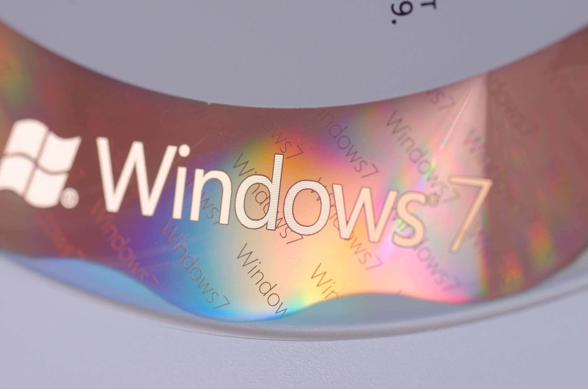 Windows 7 桌布 壁紙 — Windows 7 CD 的特寫，表面有彩虹色反射和重複文字。