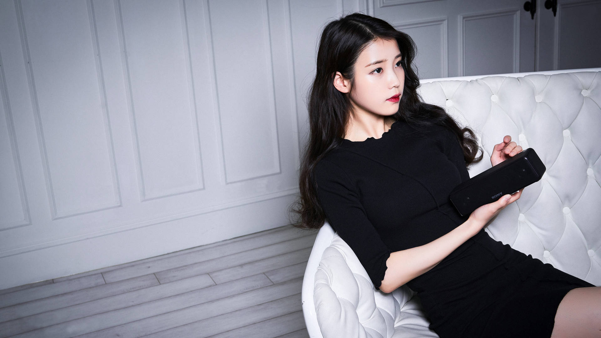 身穿黑色連衣裙的女性在現代房間的白色簇絨沙發上手持平板電腦。 — K Pop 壁紙