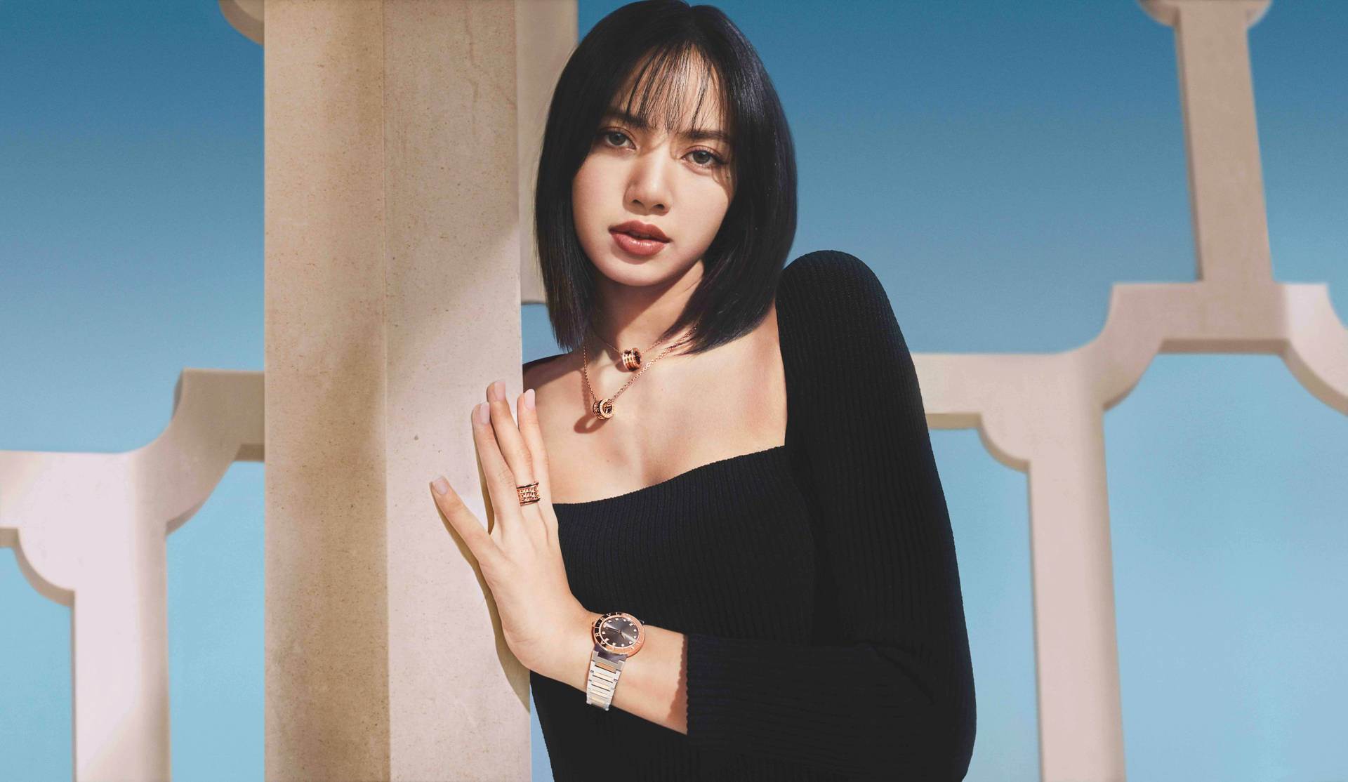 身穿黑色上衣的女性倚靠米色柱子，佩戴金色珠寶和手錶。 — Blackpink 壁紙