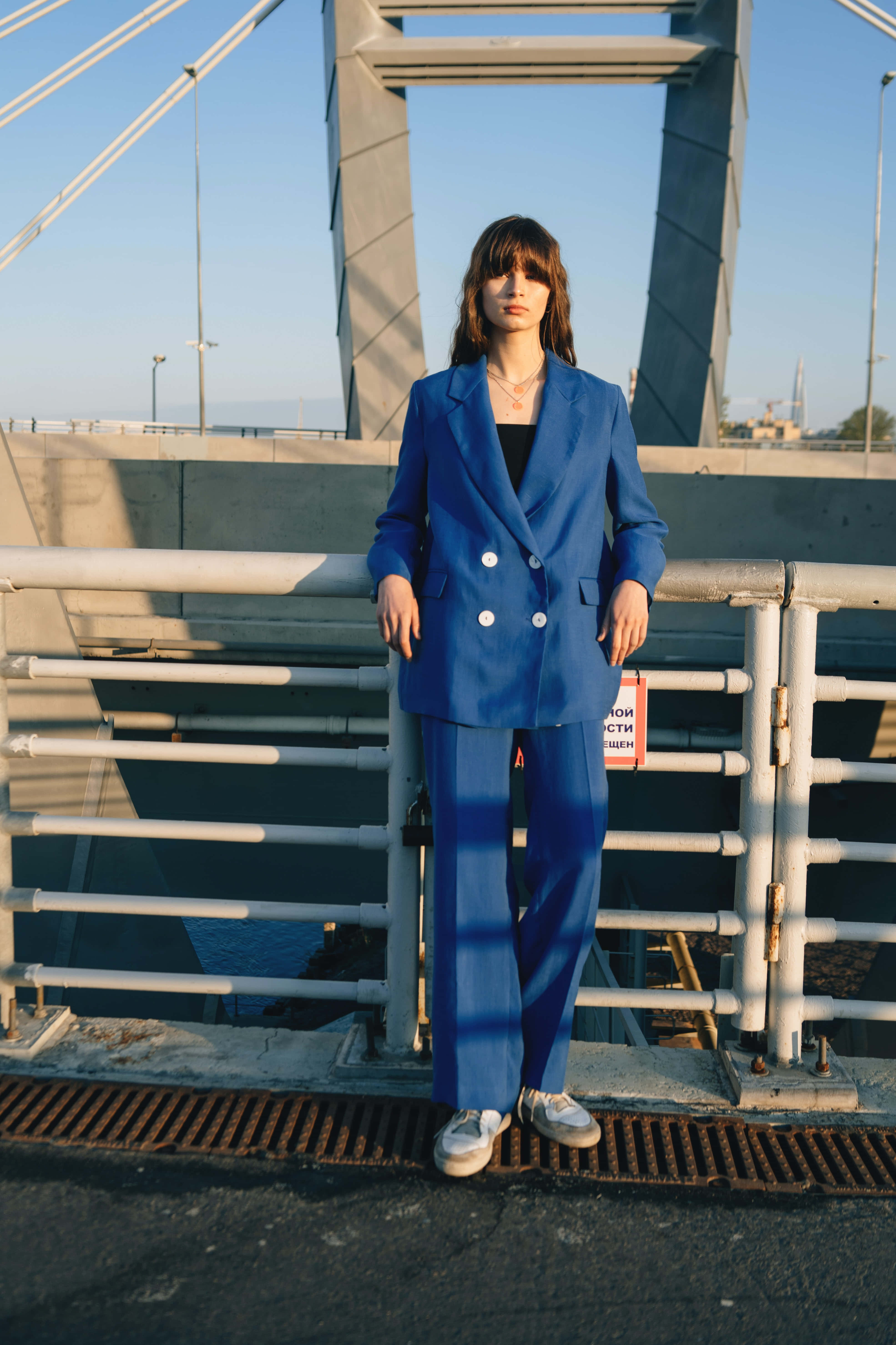 Navy Blue Blazer 桌布 壁紙 — 一位身穿大膽藍色西裝的女性自信地站在橋欄杆上，黃金時段的光線投下長長的影子。