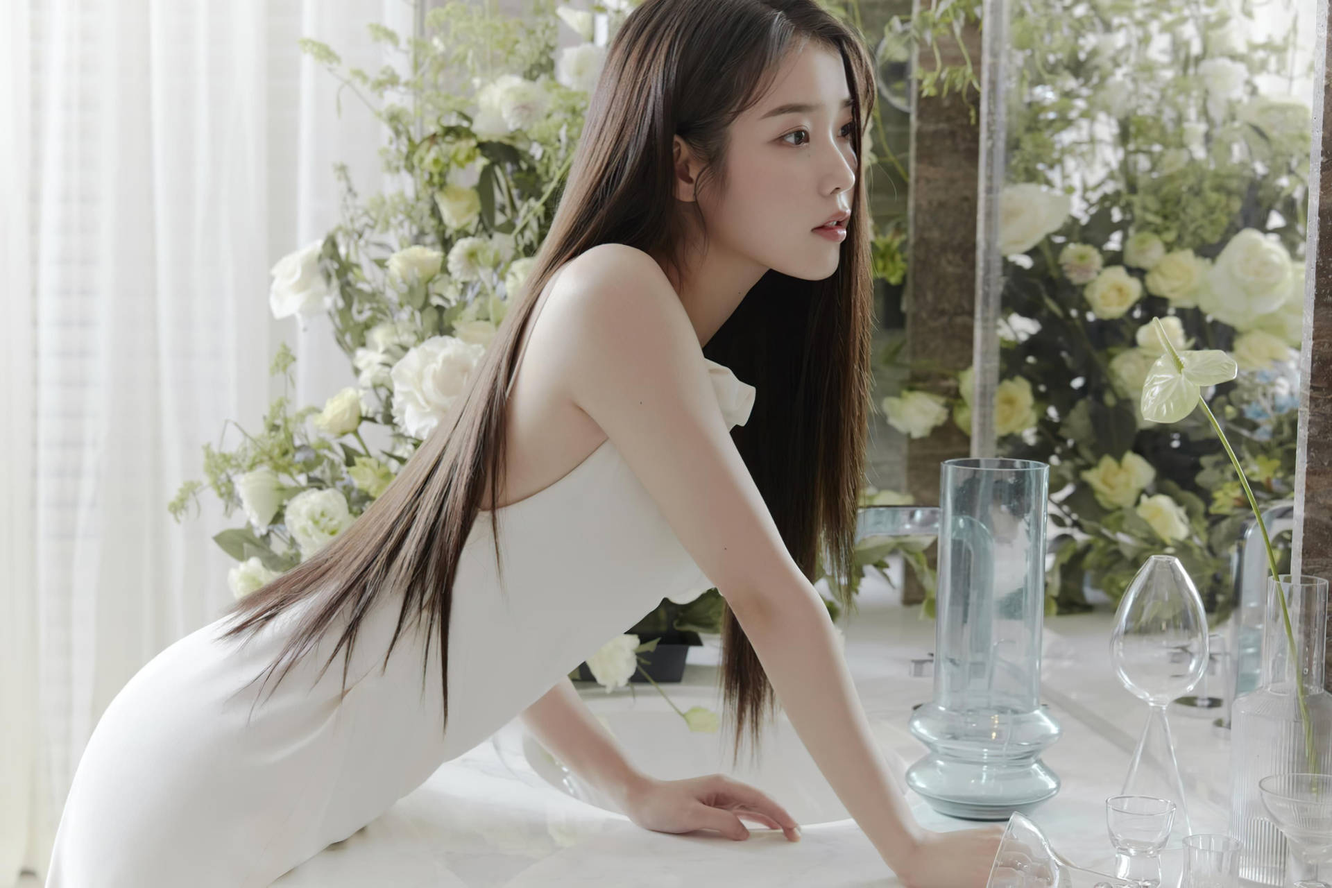 身穿白色連衣裙的女性俯身於帶有花卉裝飾的桌子上。 — K Pop 壁紙