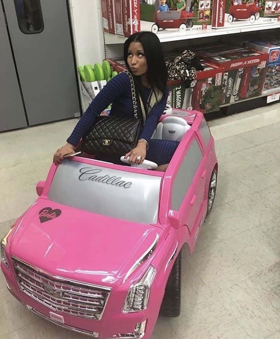  壁紙 — 一位女士自信地坐在玩具店通道內一輛亮粉紅色Barbie Cadillac玩具車上。