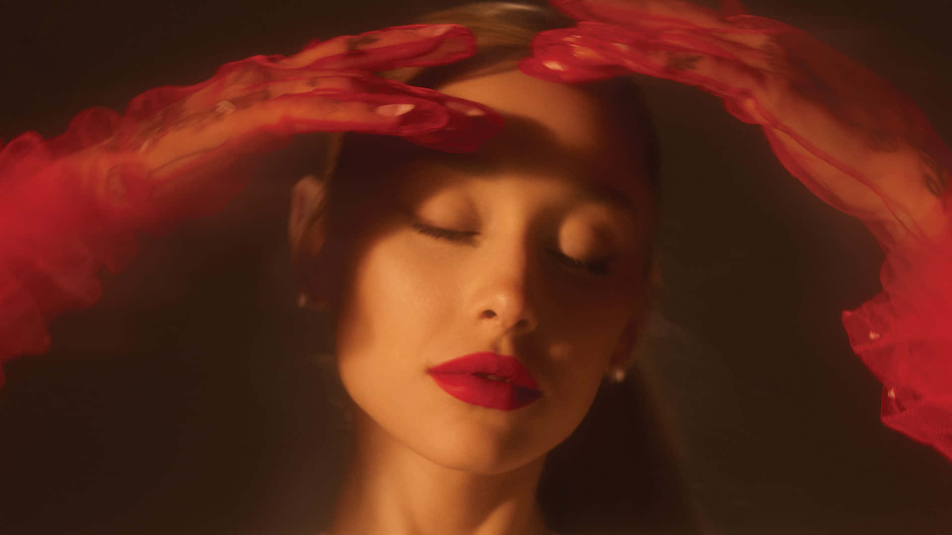  壁紙 — 一位閉著眼睛、塗著紅色唇膏的女性，戴著透視紅色手套，在溫暖昏暗的光線中勾勒出她的臉龐。