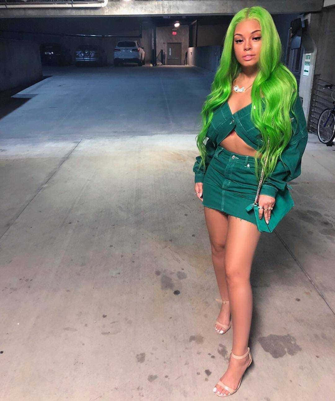  壁紙 — 一位擁有鮮豔綠色頭髮的女性自信地站在光線昏暗的地下停車場，穿著相配的綠色牛仔布套裝。