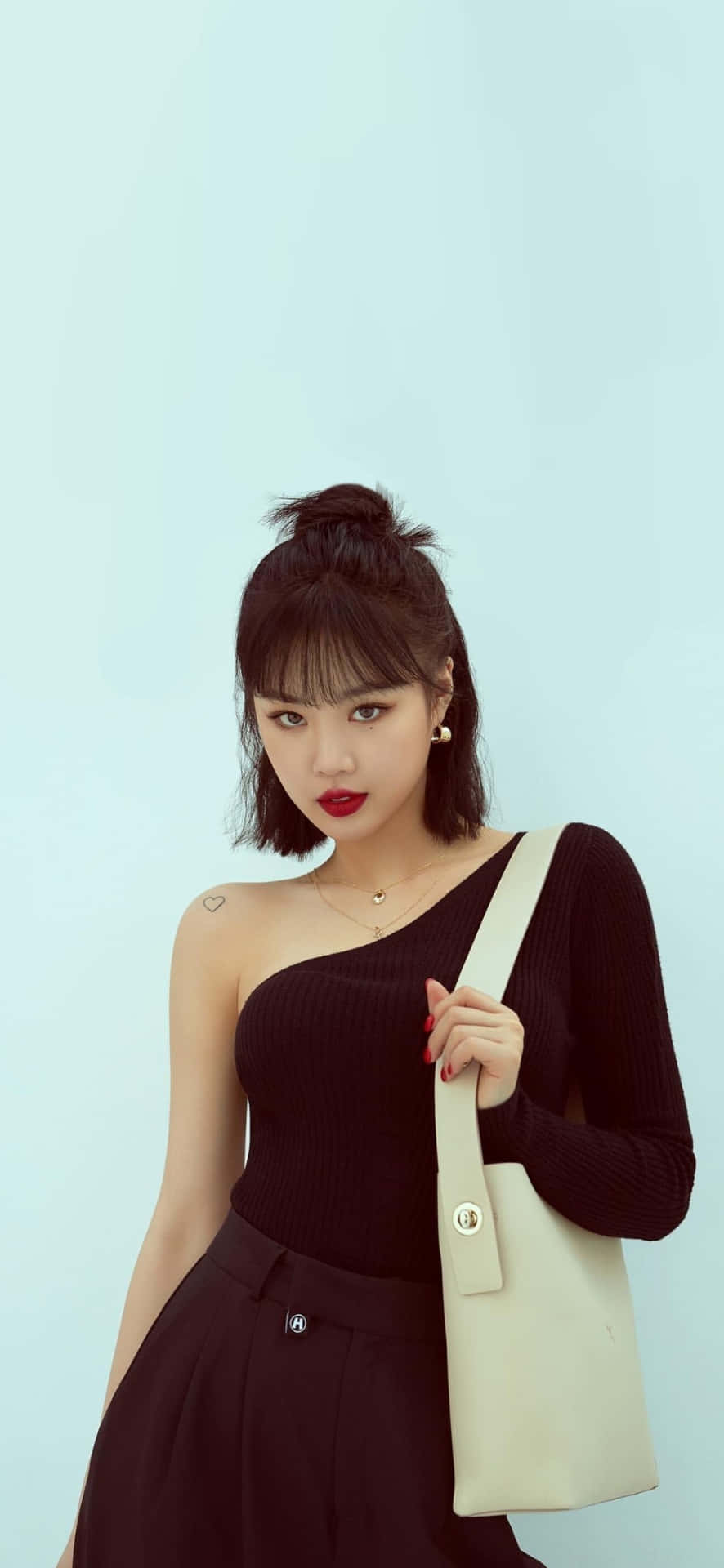  壁紙 — 一位短黑髮紅唇的女性自信地在柔和的藍色背景前擺姿勢，手持一個奶油色托特包。
