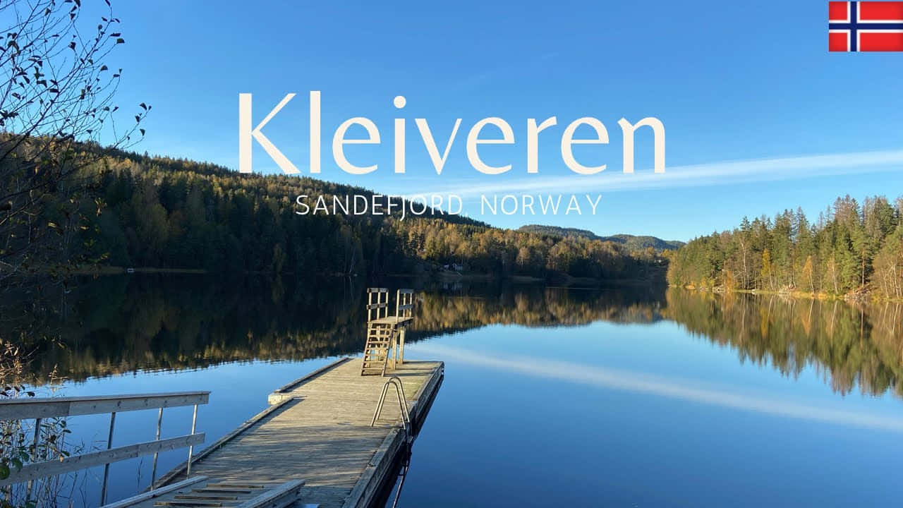 Sandefjord 桌布 壁紙 — 一個木製碼頭延伸到如鏡的湖面，倒映著挪威的秋林和清澈藍天。