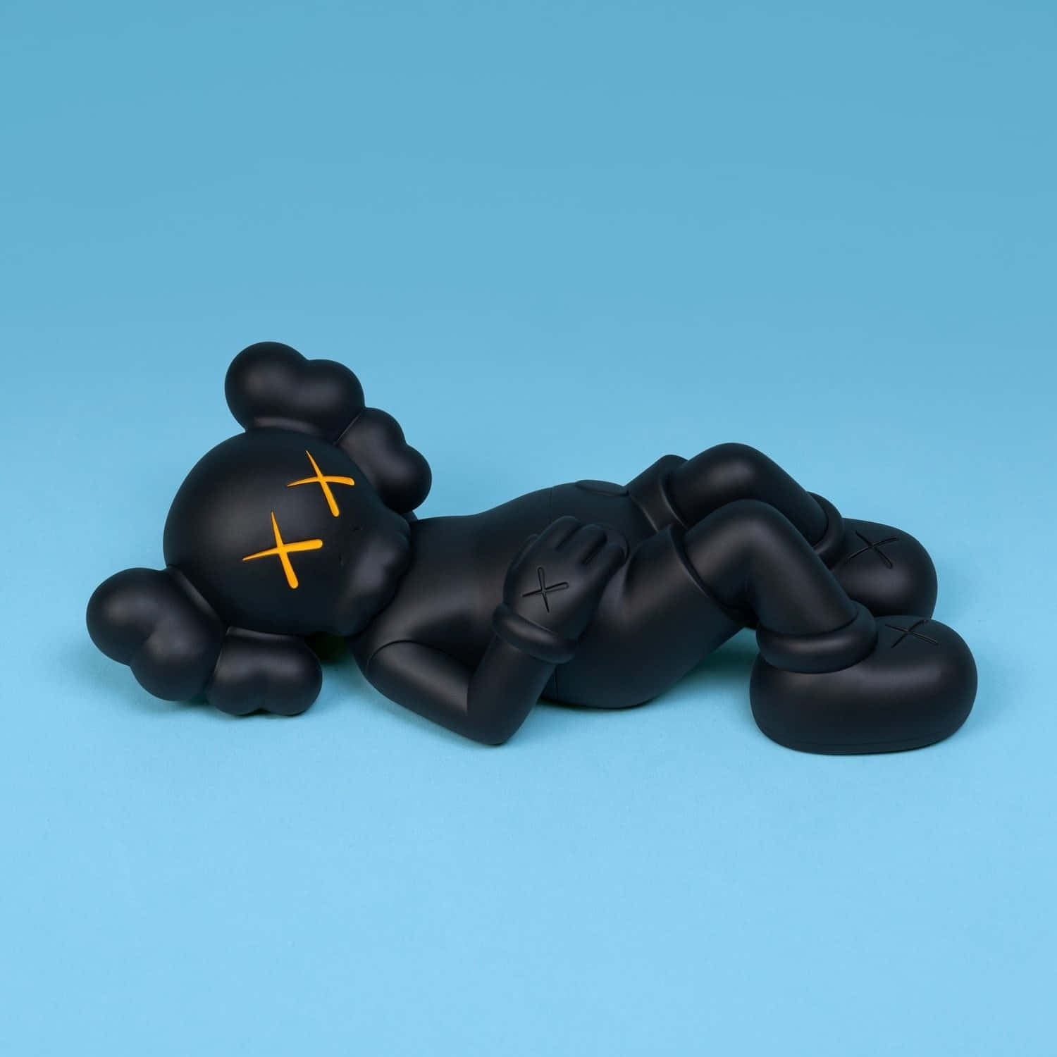  壁紙 — 一個霧面黑色的KAWS Companion公仔，帶有橙色X眼睛，放鬆地躺在純藍色背景上。