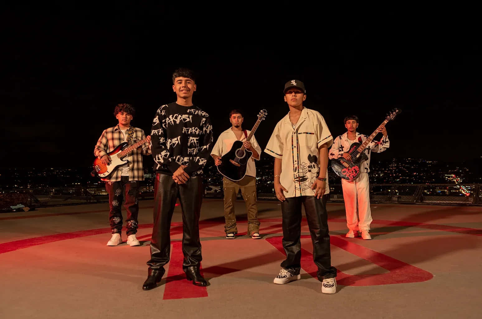  壁紙 — 五位年輕音樂家在夜晚的屋頂上自信地擺姿勢，手持吉他，背後是閃爍的城市天際線。