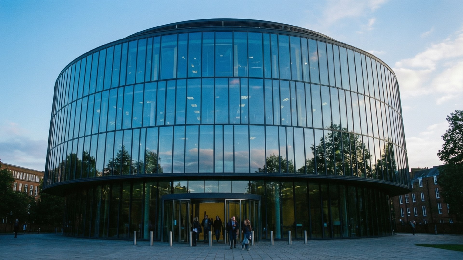 Library of Birmingham 壁紙 — 一座現代弧形玻璃建築在黃昏時分反射樹木和天空，人們正通過其旋轉門進入。