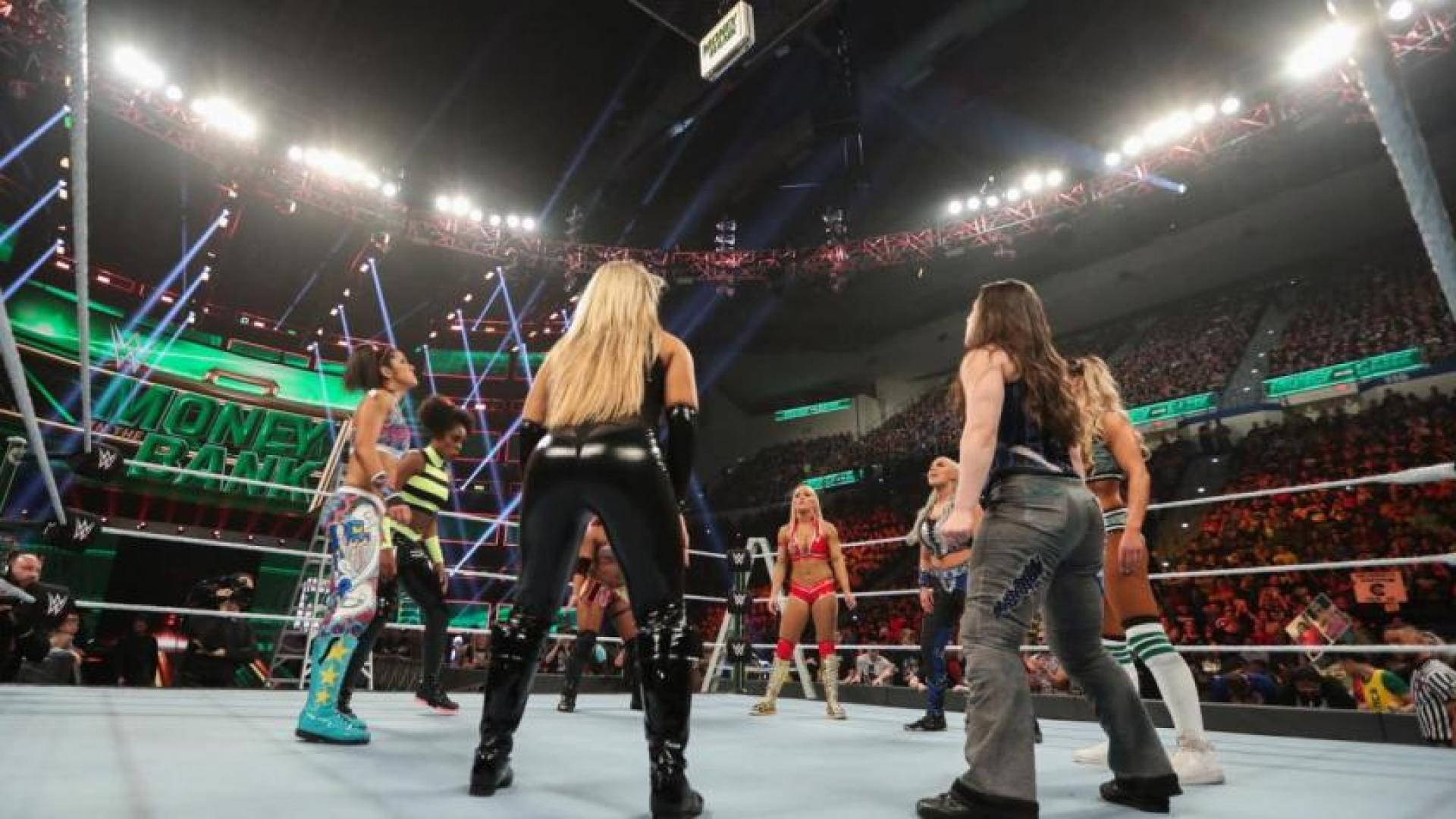 摔角 桌布 壁紙 — WWE 摔角手穿著色彩繽紛的服裝，在 Money in the Bank 活動中於燈光明亮的擂台上對峙，觀眾歡呼聲震天。