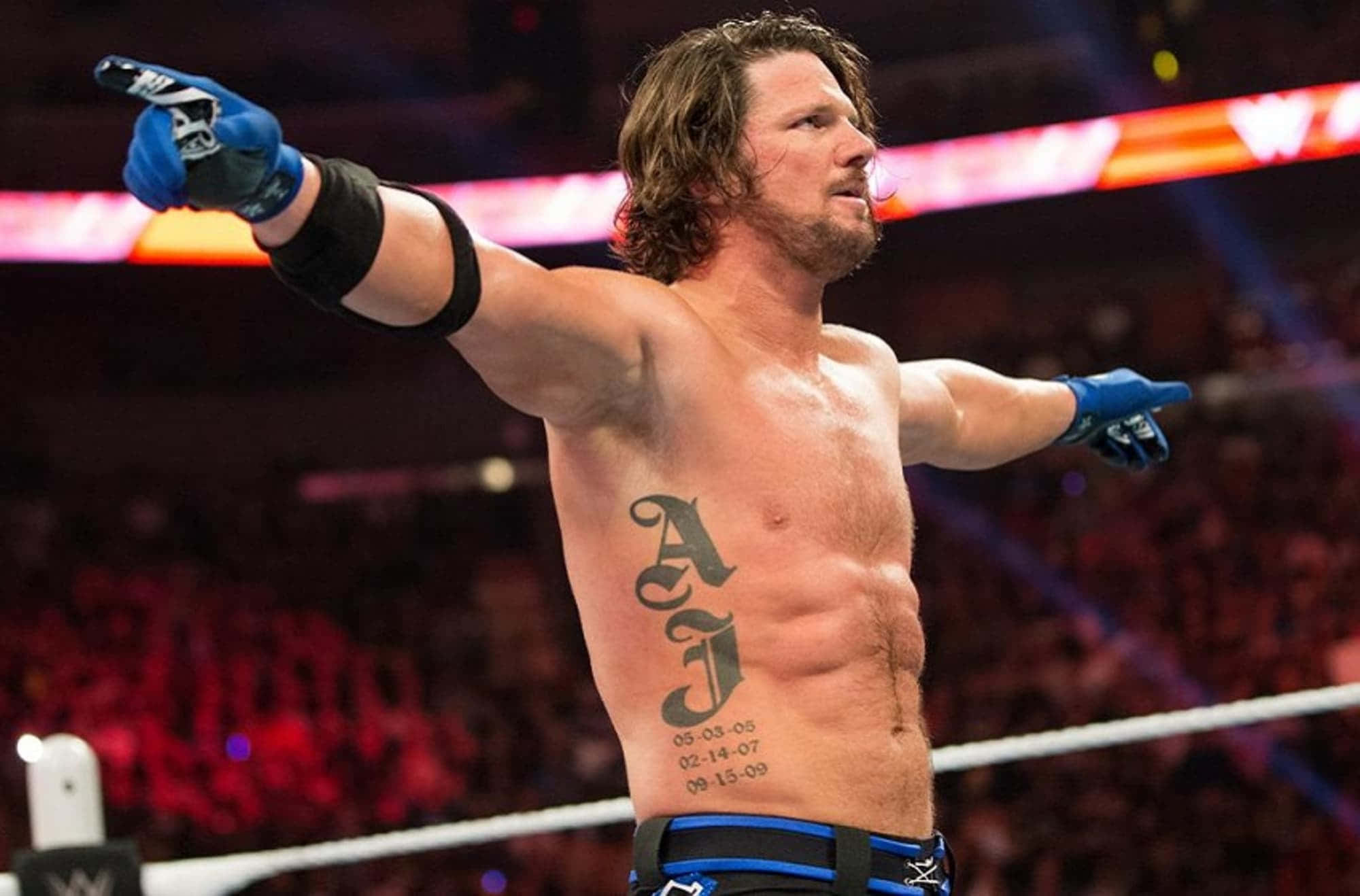 WWE 桌布 壁紙 — WWE摔角手AJ Styles在明亮的場館燈光下，雙臂伸展，展示胸前刺青，在擂台上勝利地站立。