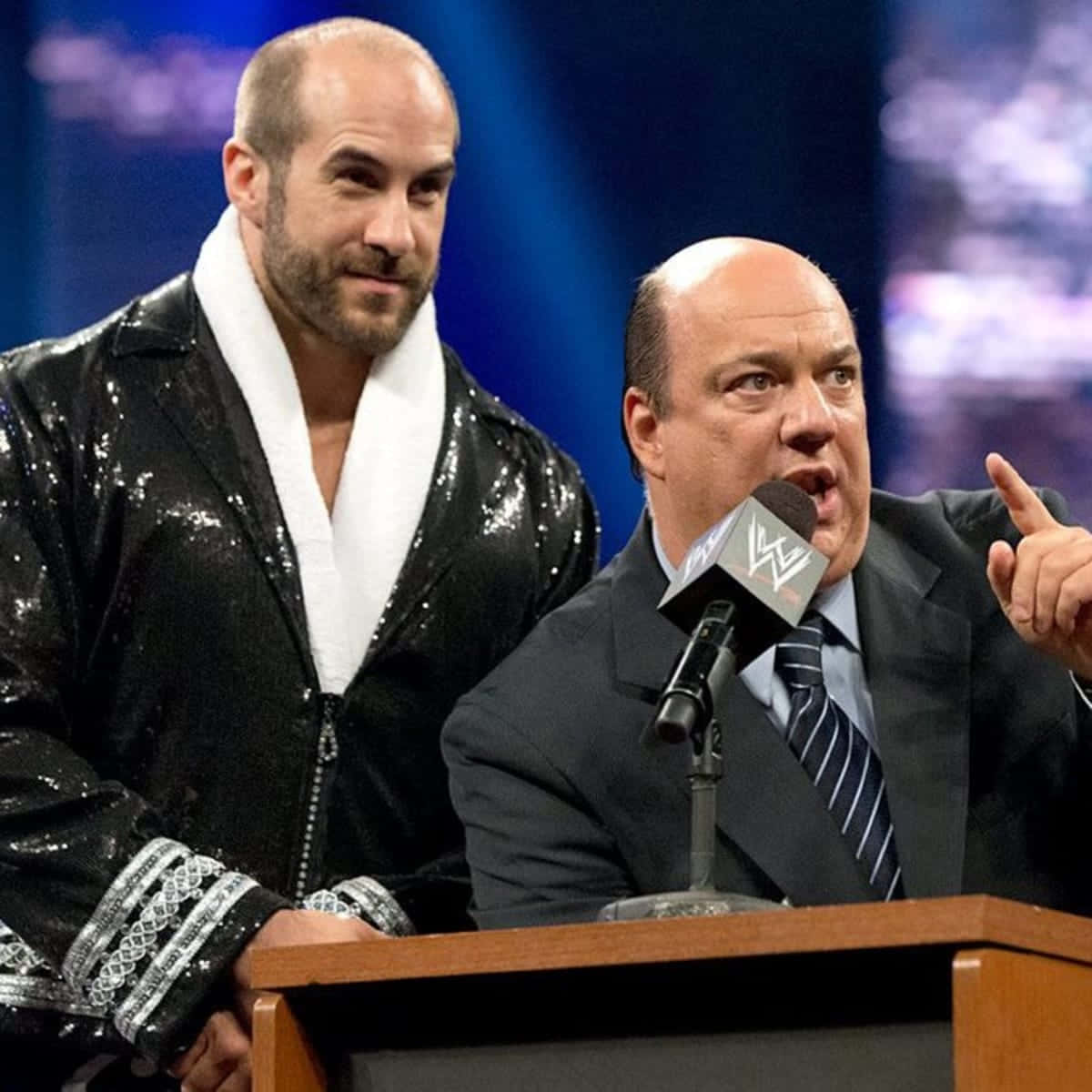 paul heyman 桌布 壁紙 — WWE摔角手Randy Orton站在Paul Heyman旁邊的講台上，Heyman在摔角活動中熱情地對著麥克風說話。