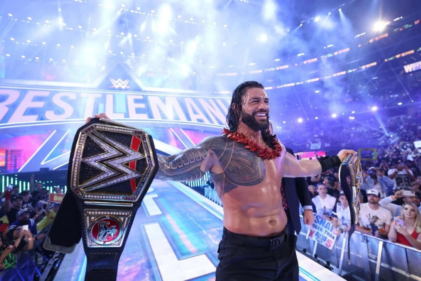 WWE 桌布 壁紙 — WWE摔角手Roman Reigns在明亮的場館燈光下，在咆哮的粉絲面前勝利地微笑，手持冠軍腰帶。