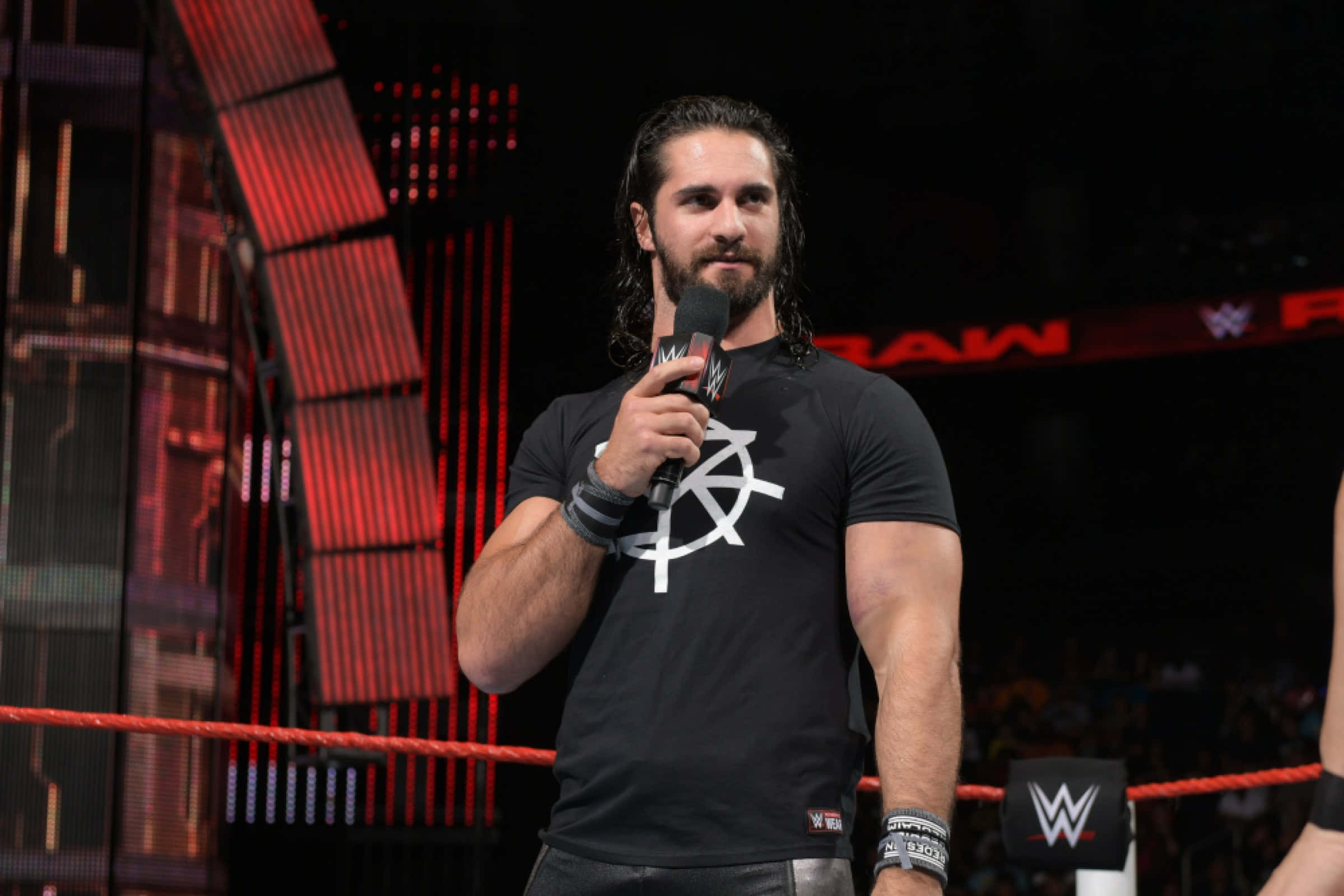 WWE 桌布 壁紙 — WWE摔角手Seth Rollins站在擂台上，在紅色舞台燈光下拿著麥克風。