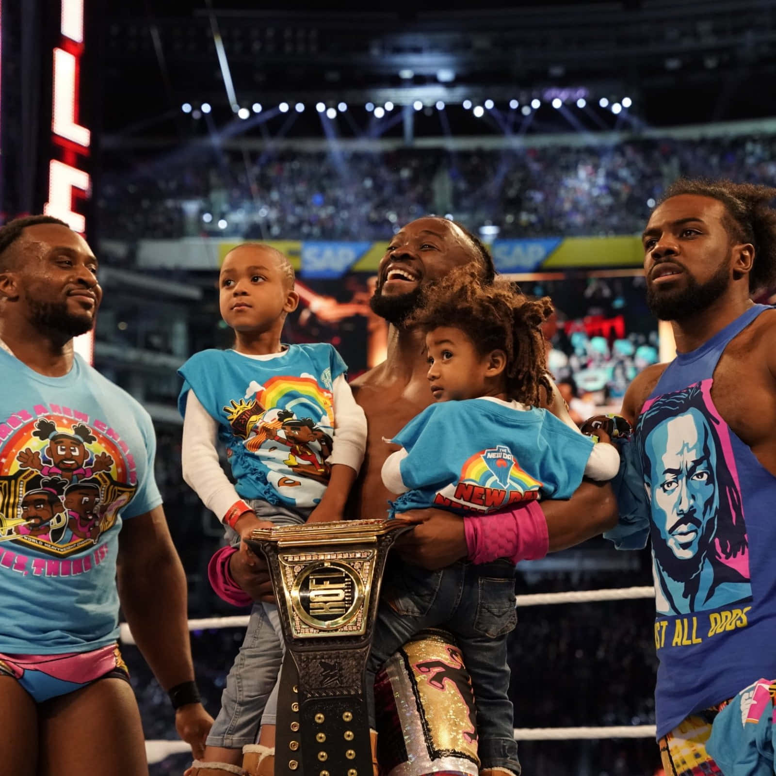 WWE 桌布 壁紙 — WWE摔角手在場館燈光下與手持冠軍腰帶的孩子們在擂台上慶祝勝利。