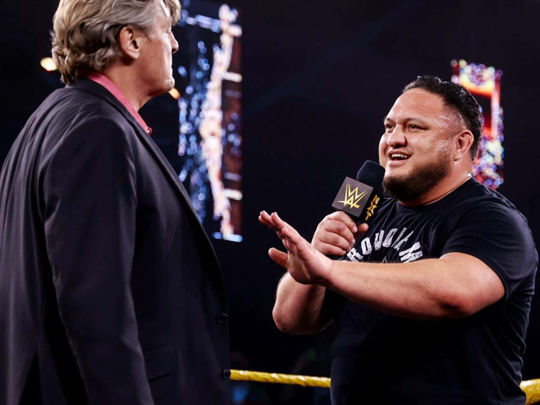 WWE 桌布 壁紙 — WWE摔角手在摔角擂台接受訪問時，手持麥克風大笑，身後有明亮的舞台燈光。