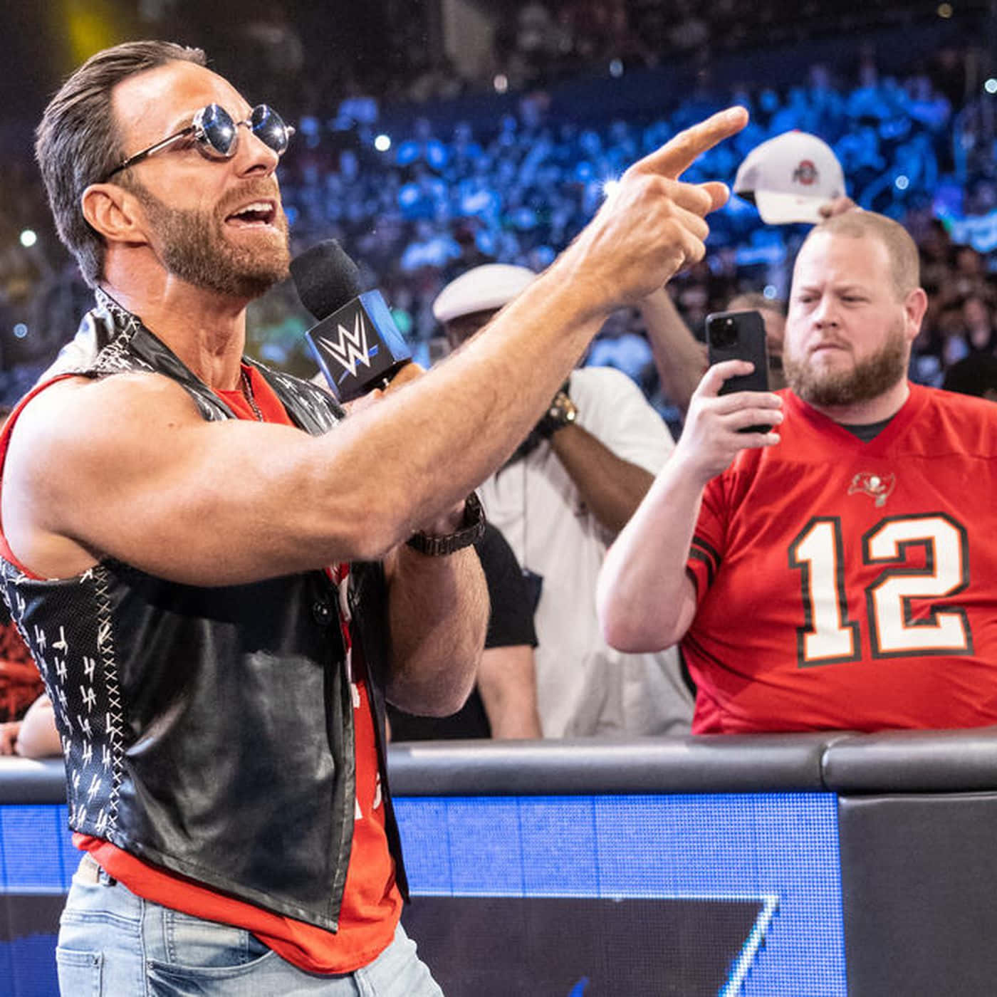 WWE 桌布 壁紙 — WWE摔角手戴著太陽眼鏡和皮背心，在現場活動中熱情地指向人群。