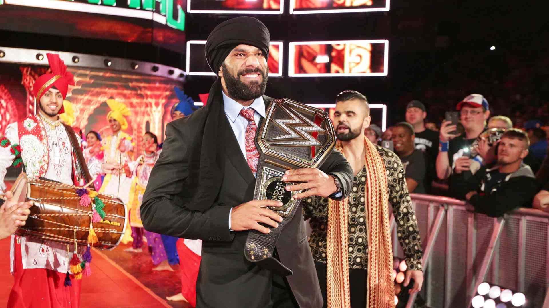 WWE 桌布 壁紙 — WWE摔角手手持冠軍腰帶，背景是傳統印度舞者和粉絲在競技場。