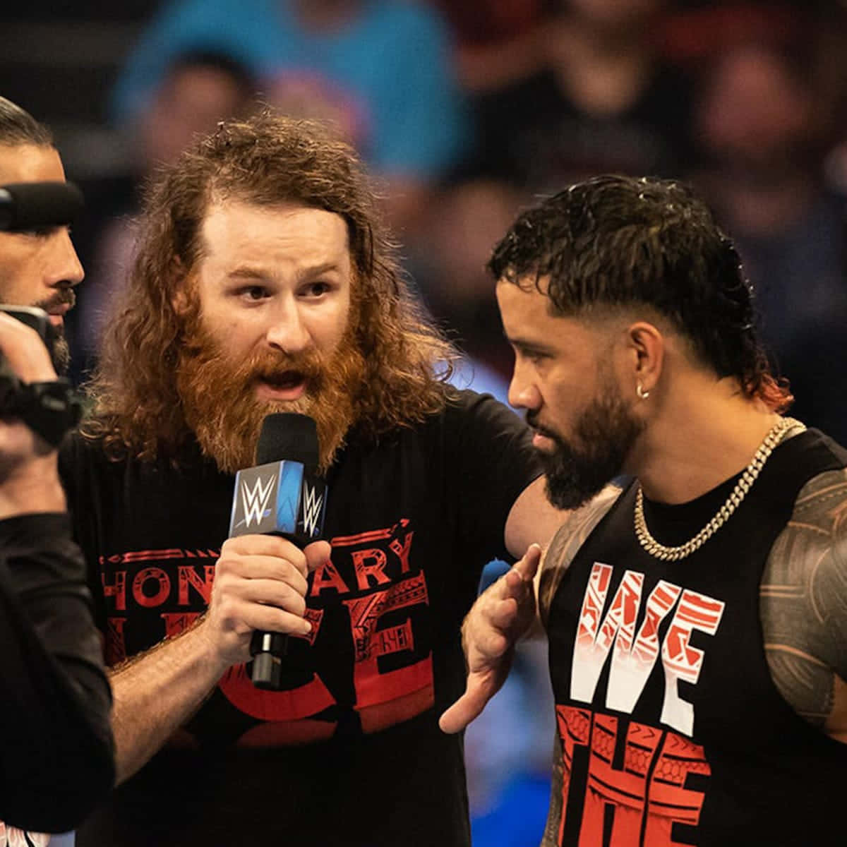 sami zayn 桌布 壁紙 — WWE摔角手留長鬍鬚，手持麥克風，在緊張的擂台訪問中與另一摔角手對峙。