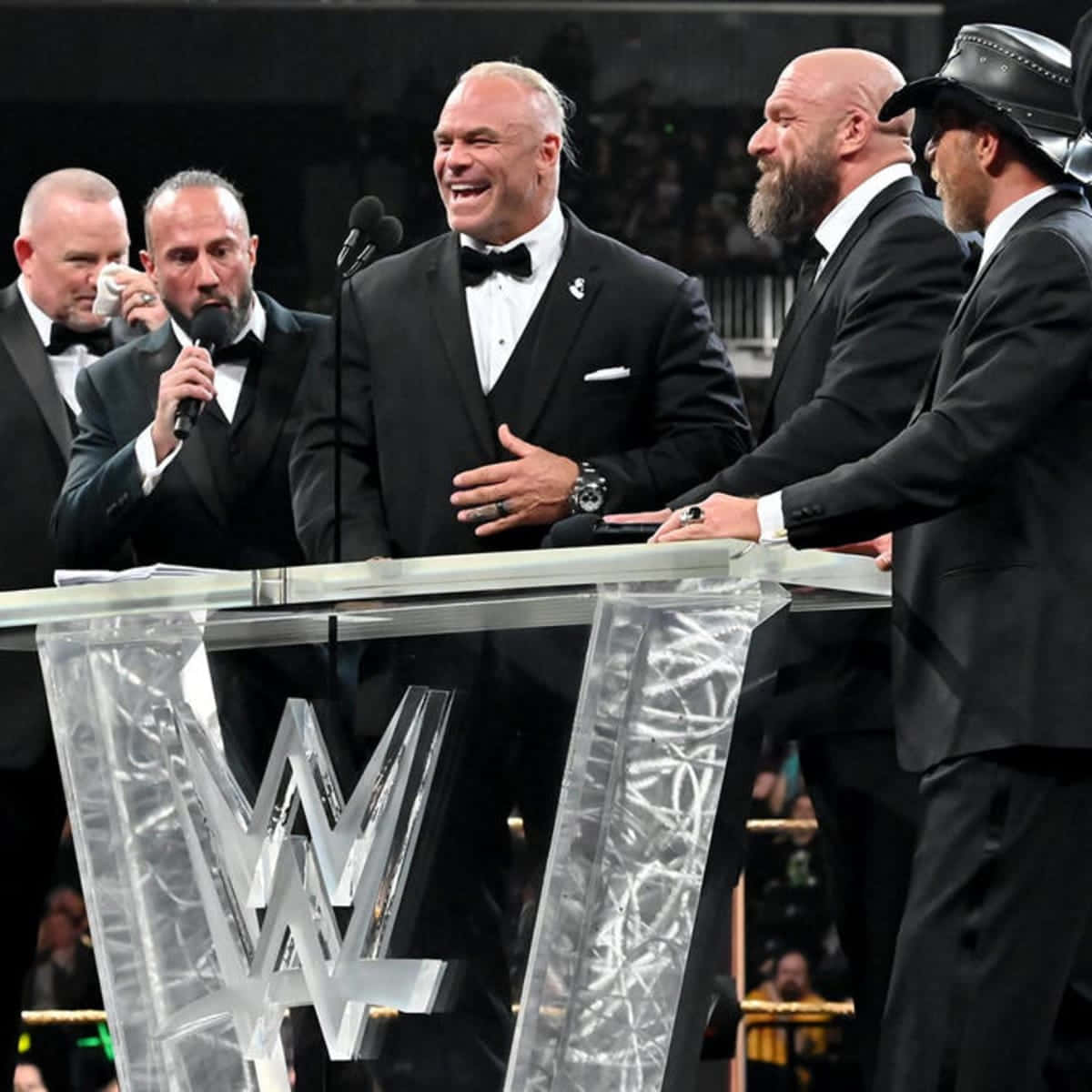 WWE 桌布 壁紙 — WWE摔角手穿著禮服，在正式活動中笑著站在一個帶有WWE標誌的透明講台周圍。