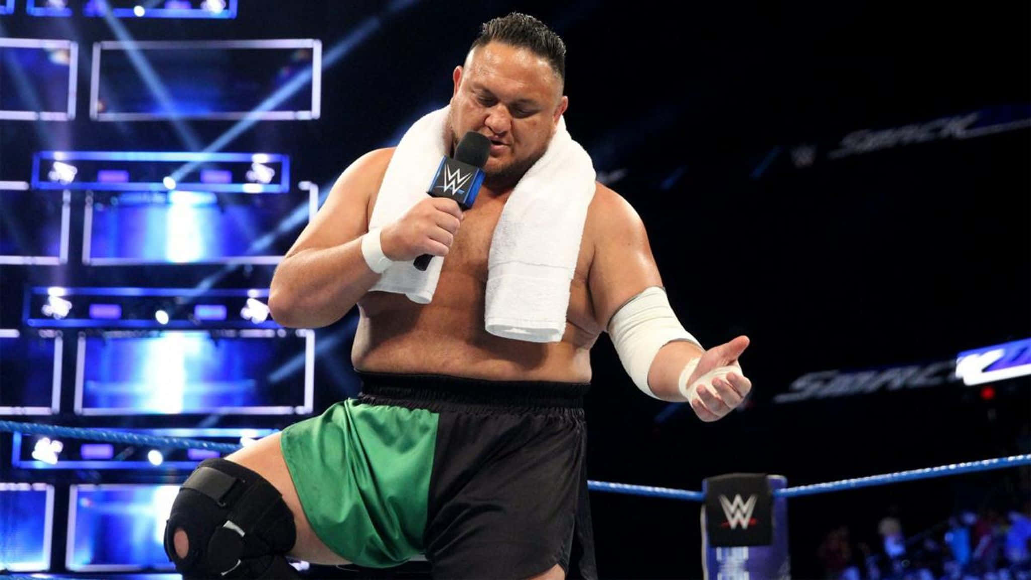WWE 桌布 壁紙 — WWE摔角手肩上搭著毛巾，在燈光明亮的擂台內對著麥克風說話。