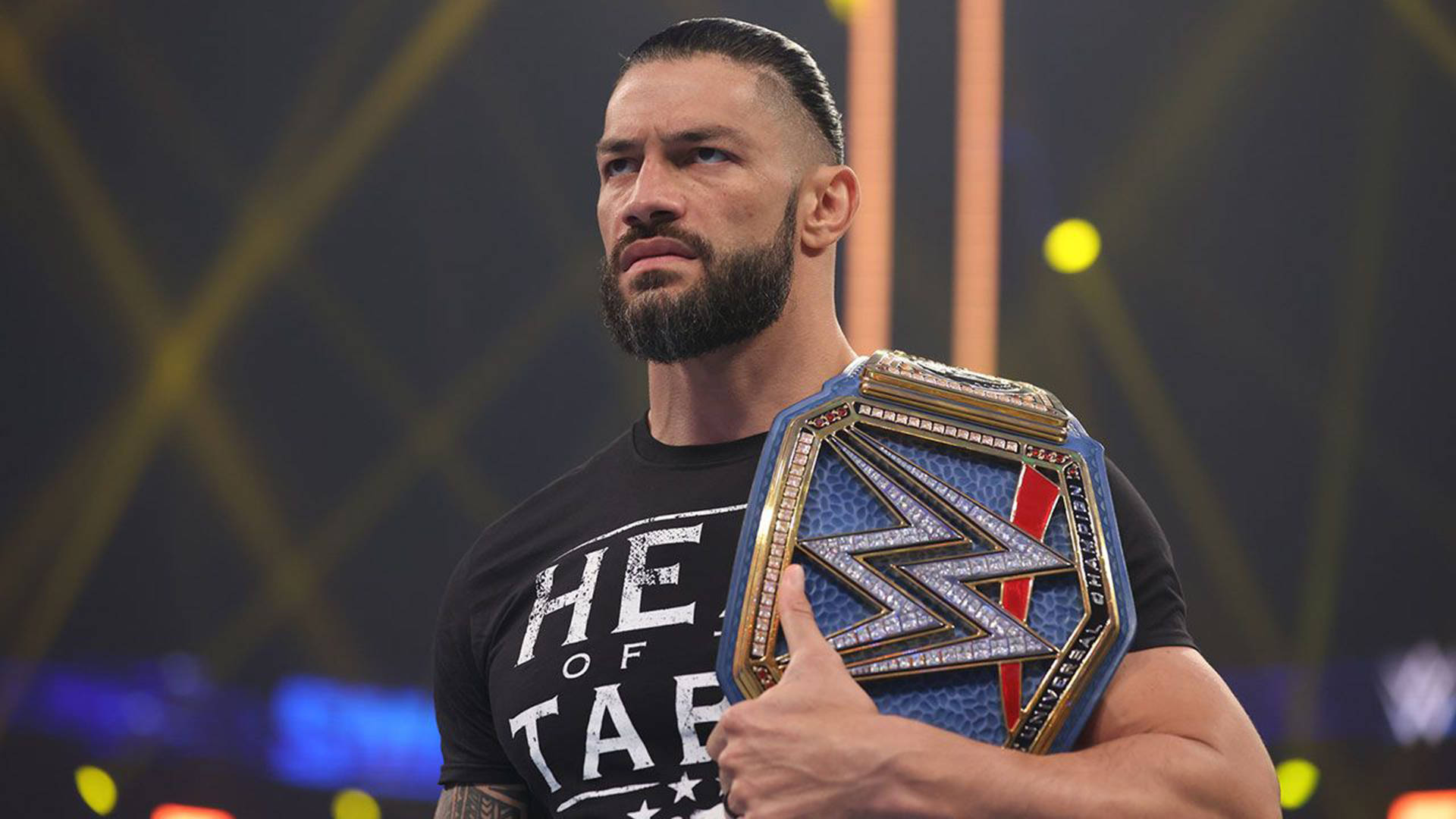 Roman 桌布 壁紙 — WWE超級巨星羅曼·雷恩斯自信地站在場館燈光下，手持他的冠軍腰帶。