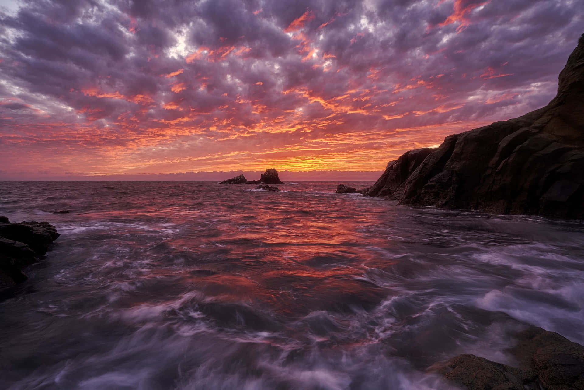 海洋上充滿活力的夕陽，伴隨著拍岸的海浪和岩石峭壁 — 美麗 壁紙
