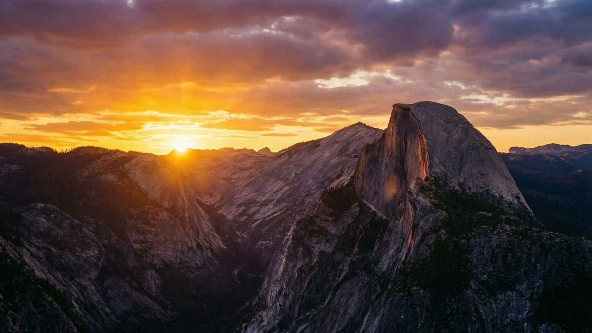 Glacier Point Sunset 壁紙 — 夕陽將半圓頂沐浴在金色光芒中，雲彩在崎嶇花崗岩山峰上空掠過天空。