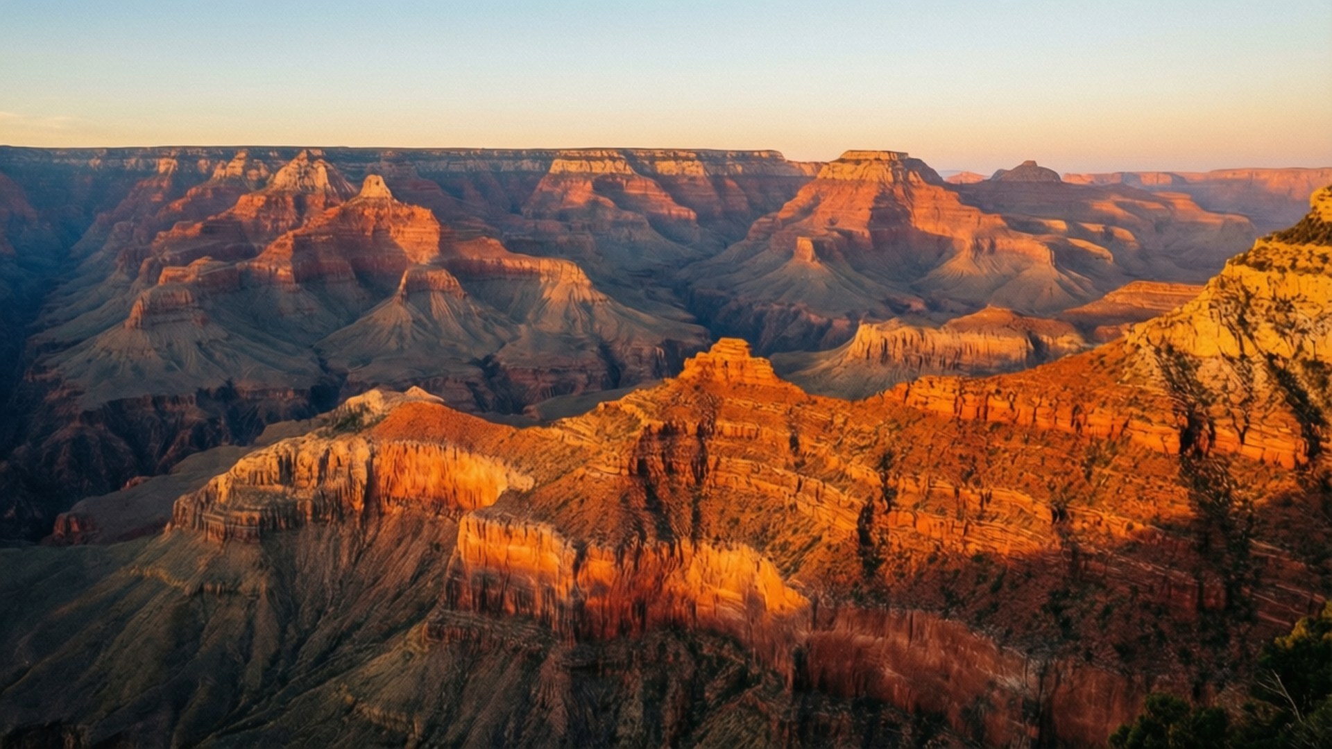 Grand Canyon Sunrise 壁紙 — 夕陽將大峽谷沐浴在溫暖的橙色光芒中，顯露出層狀岩層和深谷。
