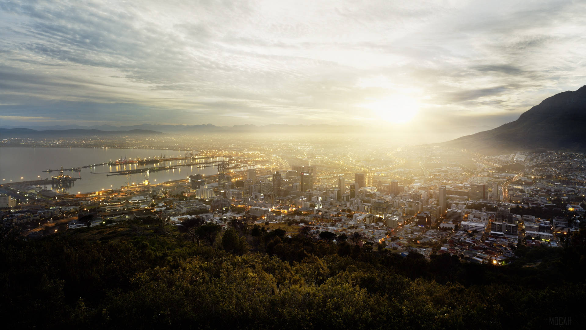 日落時分的海濱城市天際線，背景有山巒 — 4K 壁紙