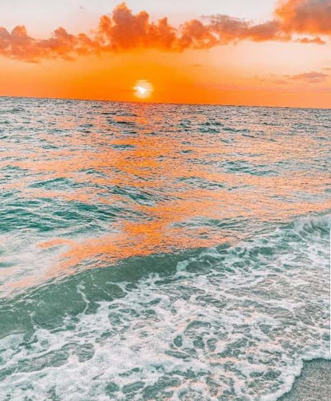  壁紙 — 夕陽將海洋染成火熱的橙色，波浪在雲層斑駁的天空下拍打著海岸。