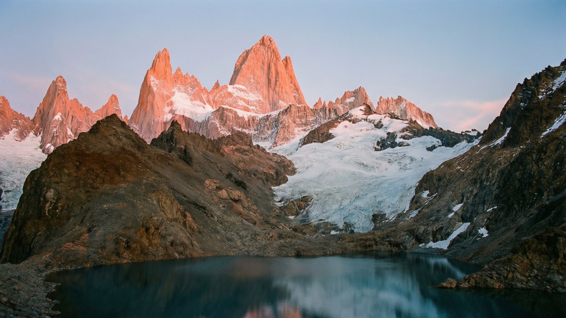 Fitz Roy Dawn 壁紙 — 夕陽將鋸齒狀的雪峰沐浴在溫暖的粉紅色光芒中，倒映在平靜的高山湖泊中。