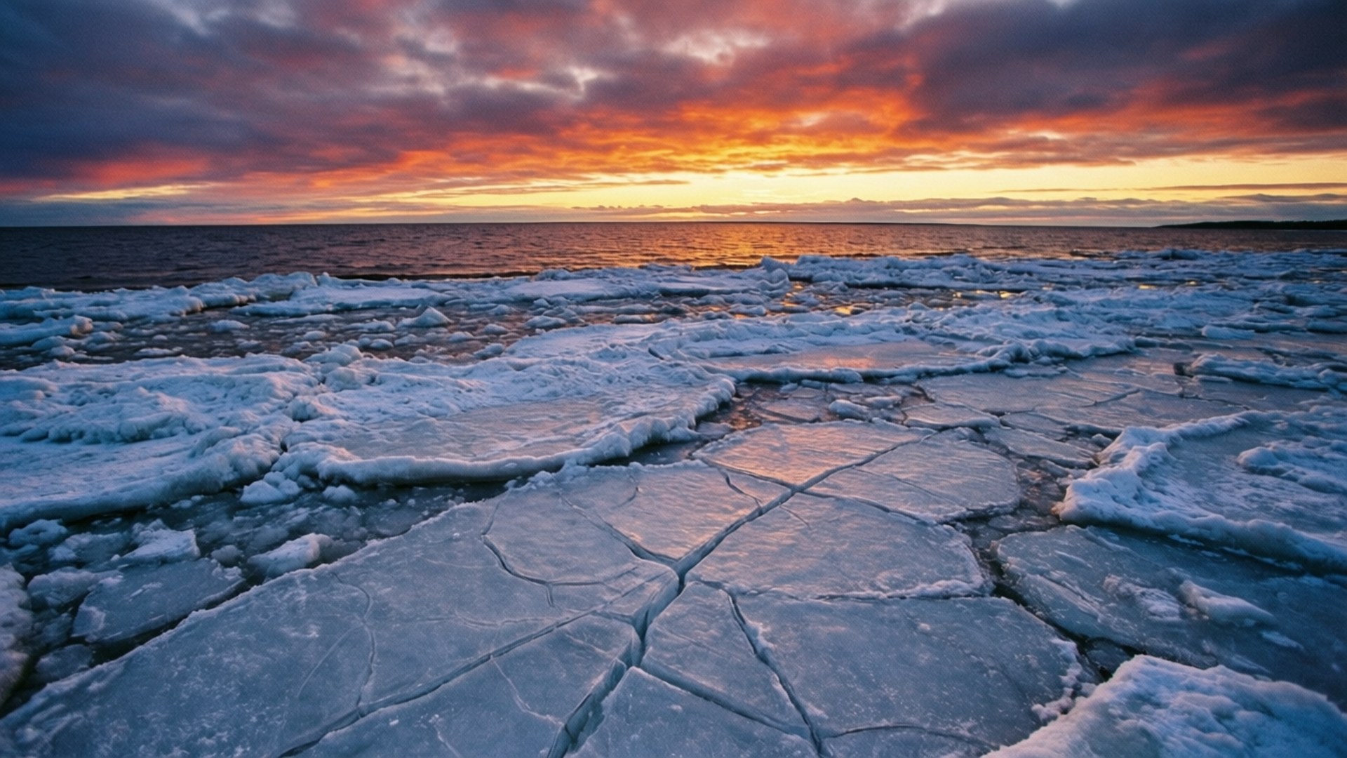 Frozen Gulf Ice Sunset 壁紙 — 夕陽將天空染成火熱的橙色和紫色，裂開的冰塊在冰封的海面上閃閃發光。
