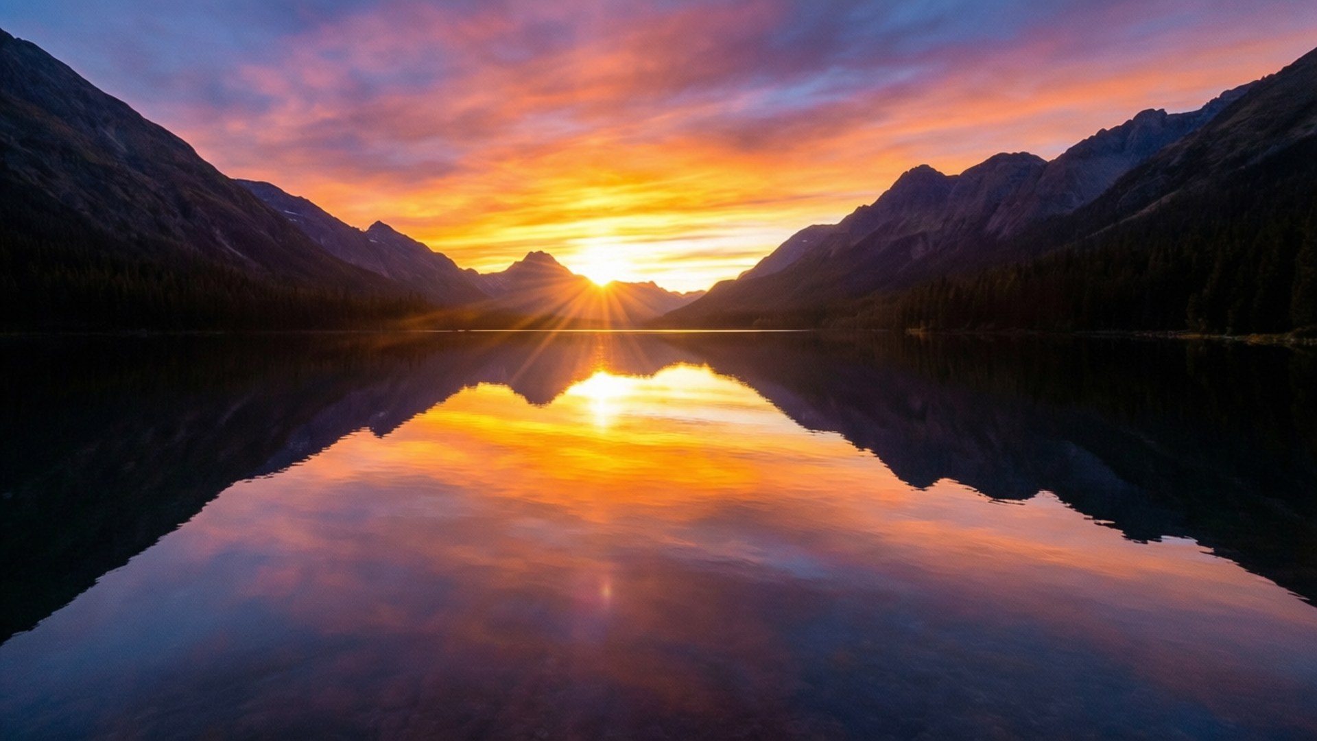 Mountain Lake Sunset Reflection 壁紙 — 夕陽散發出金色的光芒，映照在平靜的湖面上，湖面倒映著山脈，天空如火般絢麗。