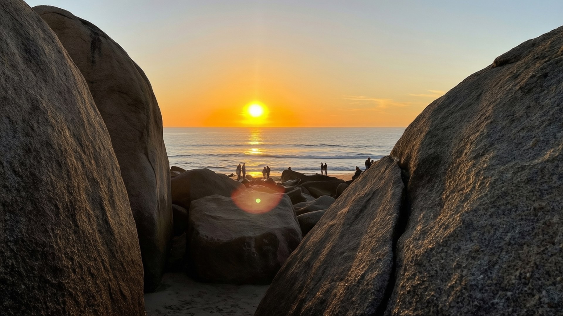 Clifton Beach Sunset 壁紙 — 夕陽在巨石之間閃耀，剪影般的人們沿著海灘漫步。