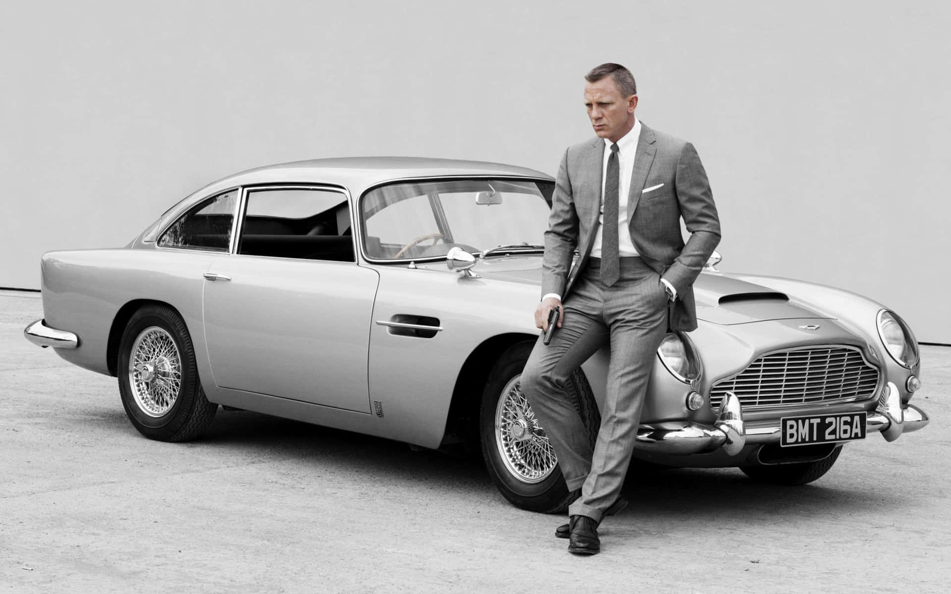  壁紙 — 一名身穿筆挺西裝的男子自信地靠在一輛經典銀色Aston Martin DB5上，手持槍支。