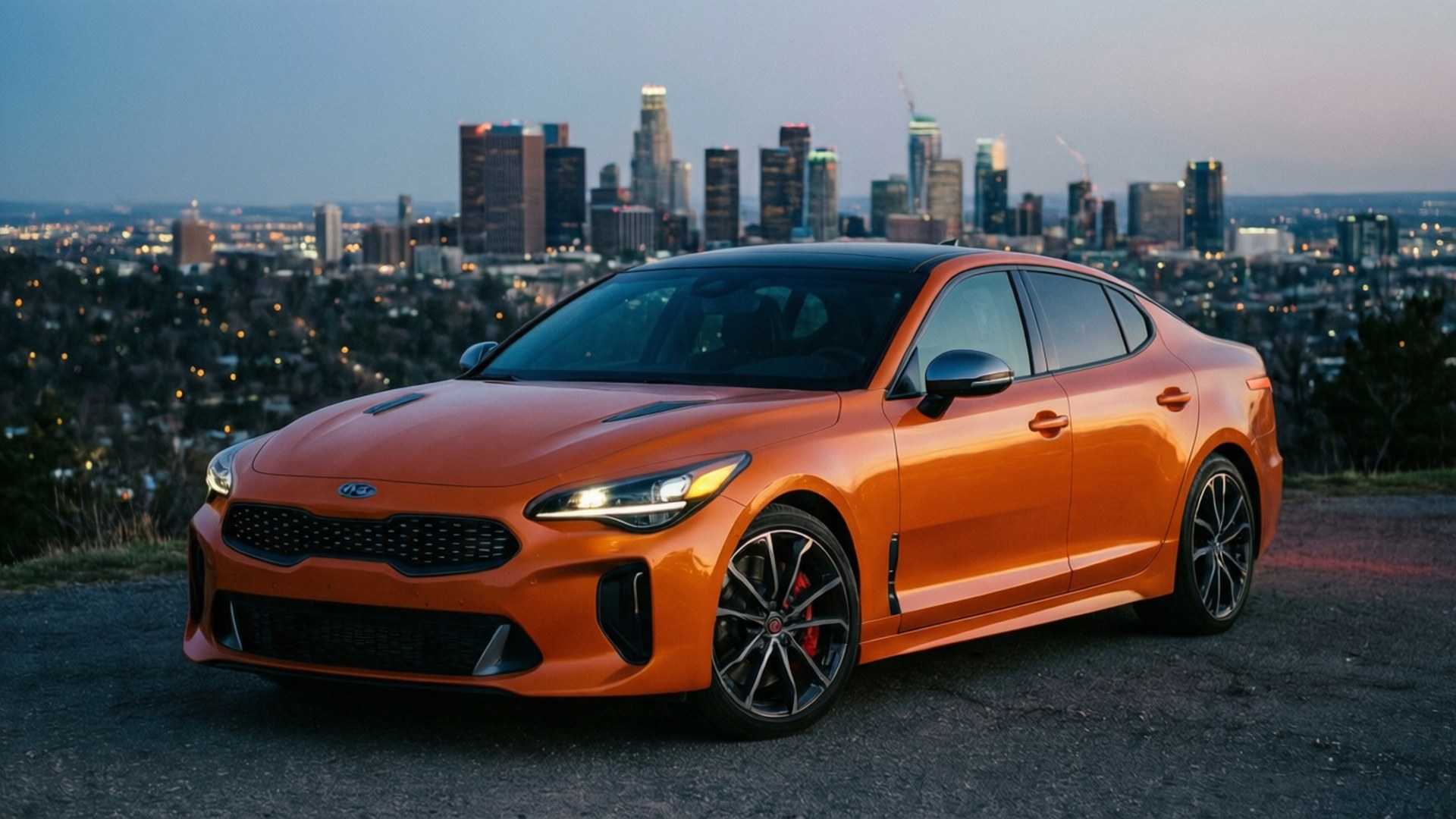 Stinger City Lights 壁紙 — 一輛鮮橙色的Kia Stinger運動轎車停泊在山頂，俯瞰黃昏時分廣闊的城市天際線。