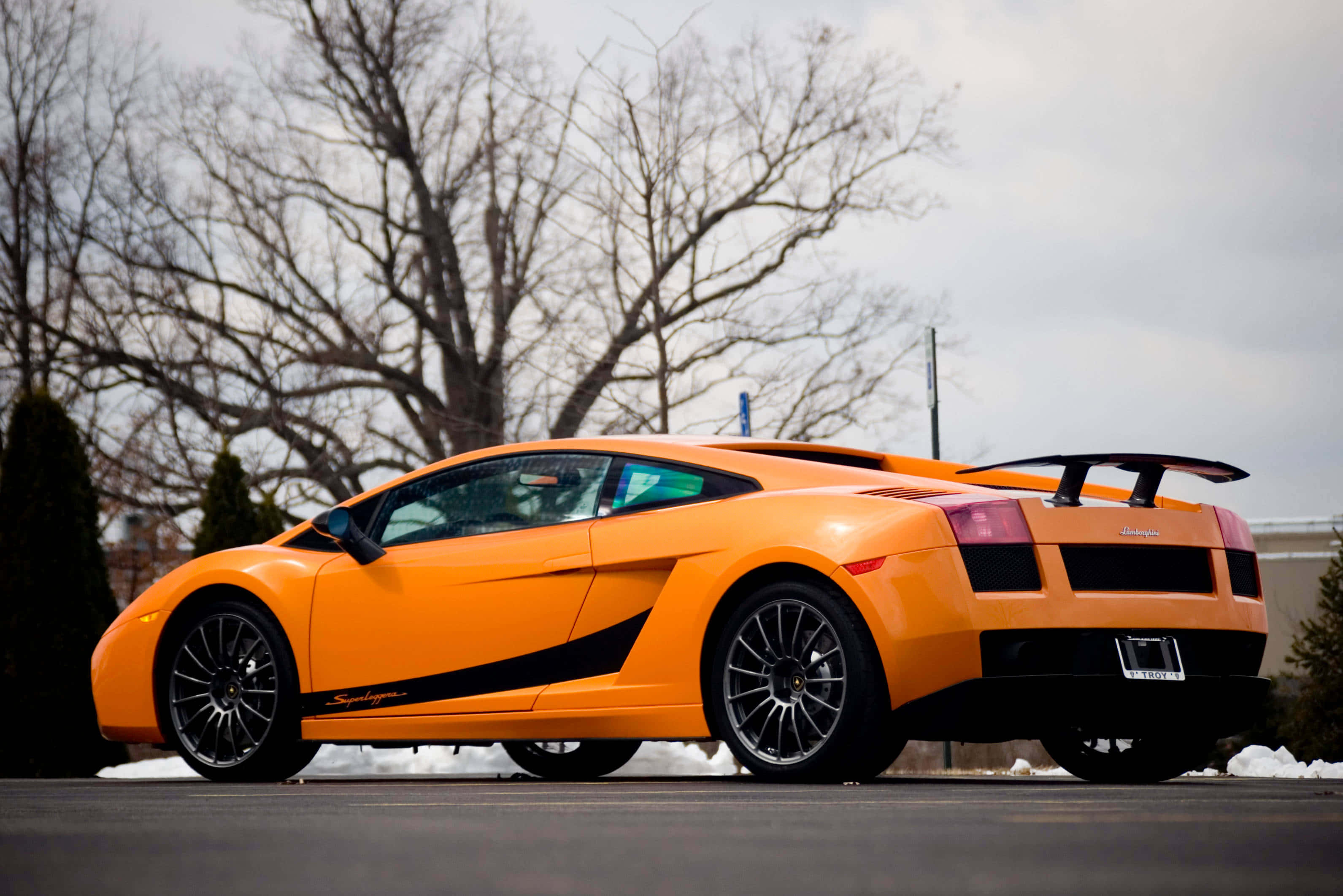 Lamborghini Gallardo 桌布 壁紙 — 一輛鮮橙色的藍寶堅尼 Gallardo Superleggera 停放在積雪的瀝青停車場，背景有光禿禿的樹木。