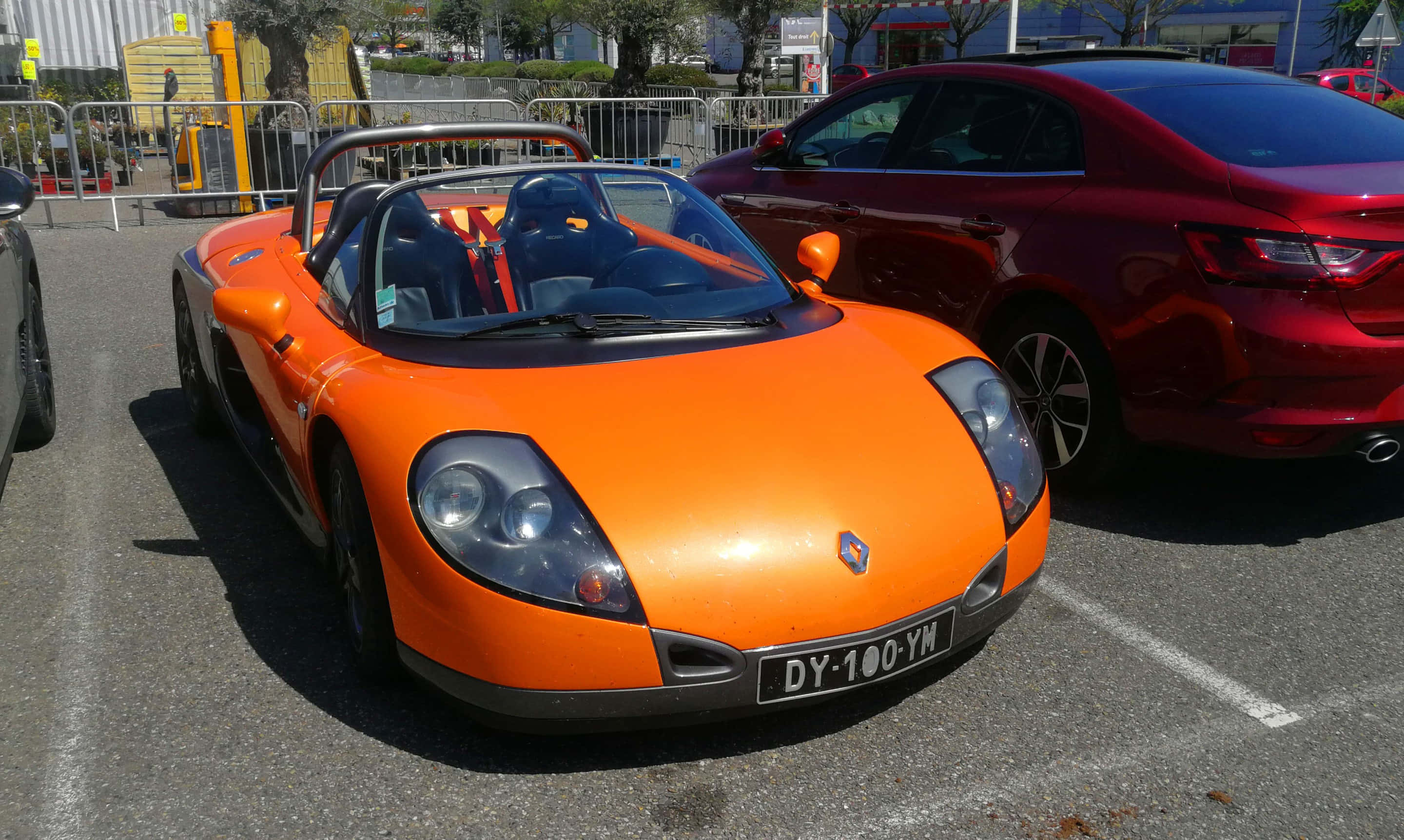 Renault Sport Spider 桌布 壁紙 — 一輛鮮橙色的雷諾Spider跑車在白天停放在戶外停車場，旁邊有一輛紅色轎車。