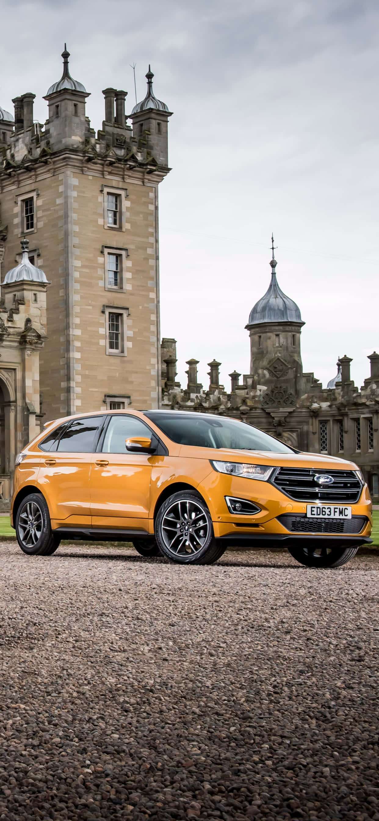 Ford Edge 桌布 壁紙 — 一輛鮮橙色SUV停放在歷史石城堡前的碎石地上，天空多雲。