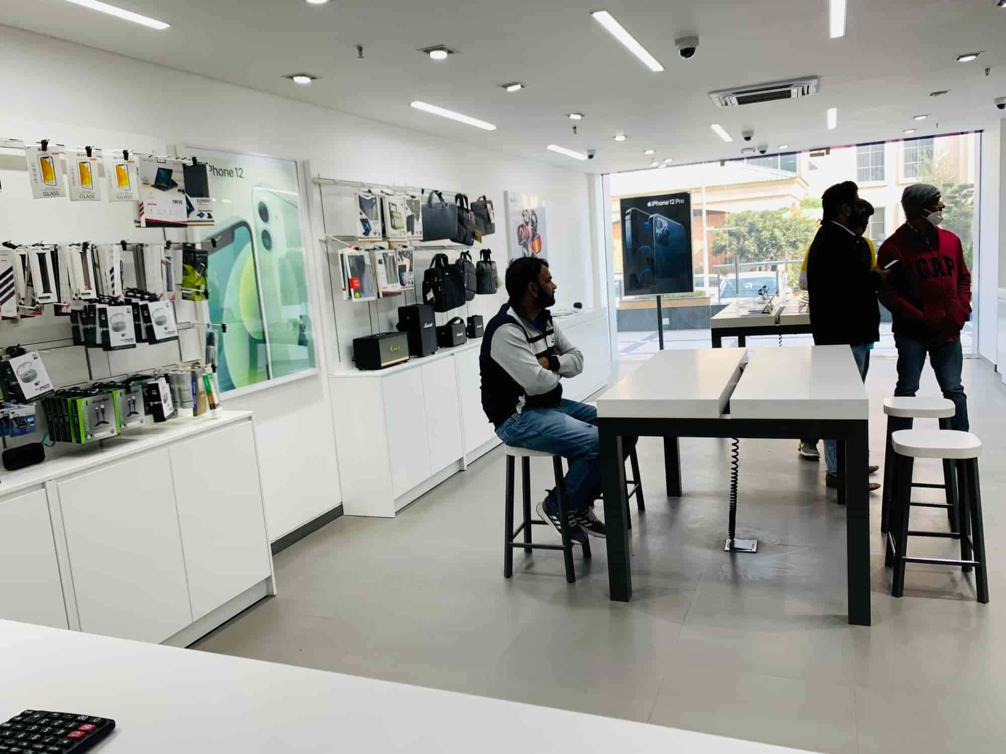 Apple Store 桌布 壁紙 — 現代科技店內部，顧客在明亮的螢光燈下瀏覽白色展示架和桌子上的產品。