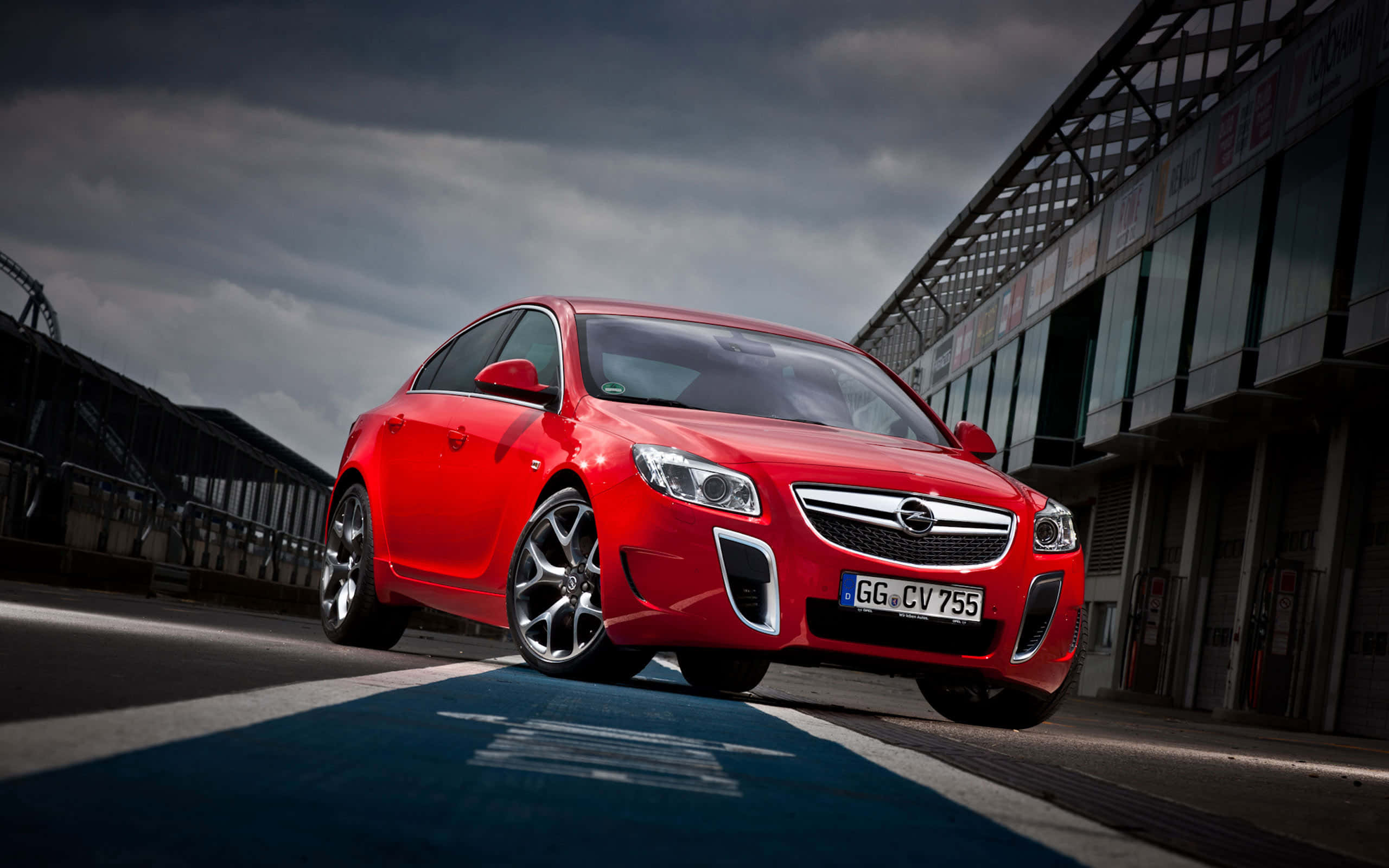Opel Insignia 桌布 壁紙 — 一輛鮮紅色的歐寶Insignia OPC停放在賽道上，天空烏雲密佈，氣氛戲劇化。