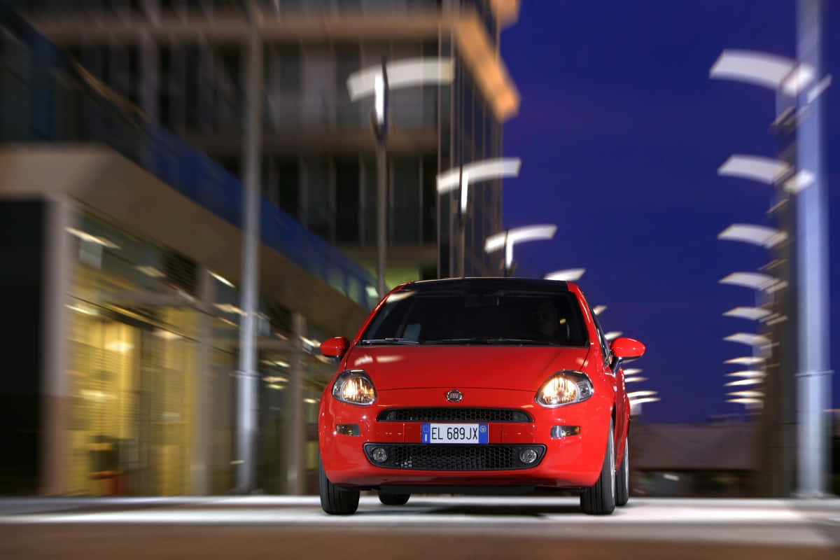 Fiat Punto 桌布 壁紙 — 一輛鮮紅色的Fiat 500在夜間的城市街道上飛馳，模糊的燈光劃過。