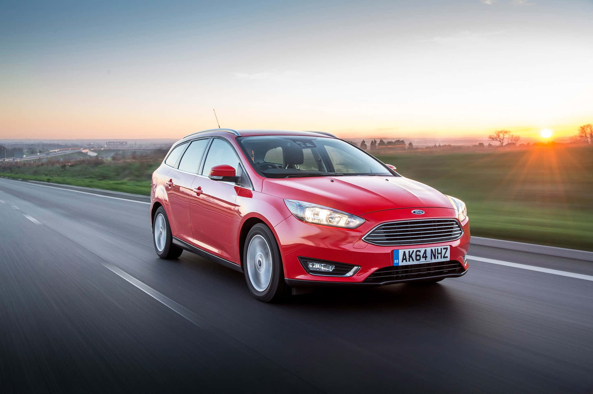 Ford Focus 桌布 壁紙 — 一輛鮮紅色的福特福克斯旅行車在日落時分的高速公路上疾駛，金色光芒在車後閃耀。