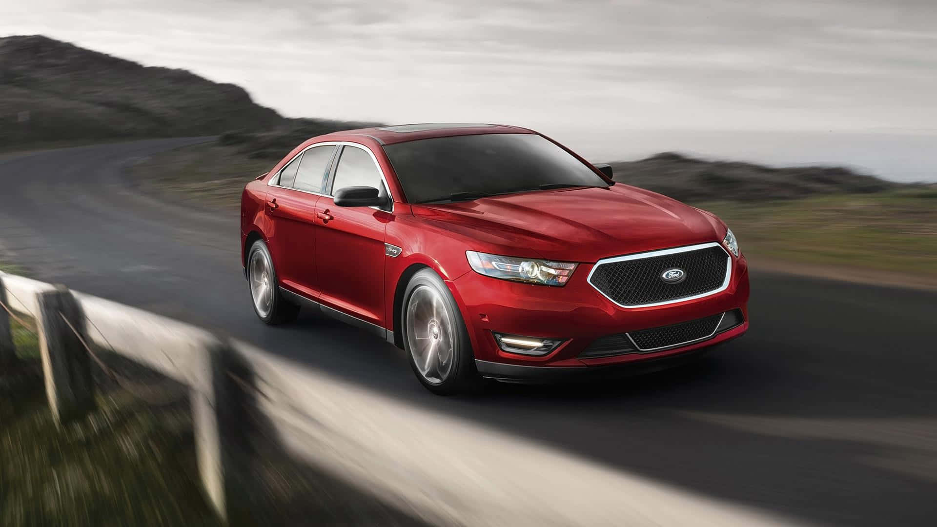 Ford Taurus 桌布 壁紙 — 一輛鮮紅色的福特 Taurus 房車在蜿蜒的山路上疾馳，帶有模糊的動感和陰天。