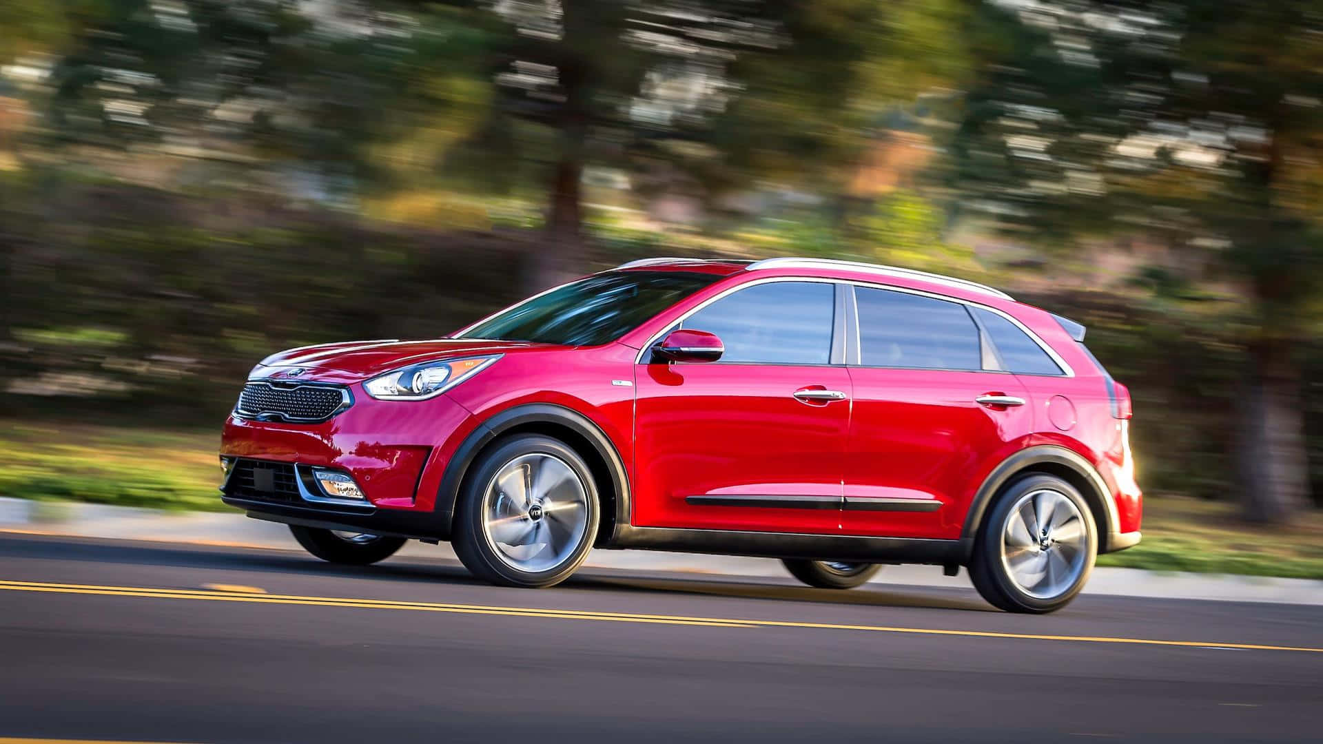 Kia Niro 桌布 壁紙 — 一輛鮮紅色的起亞SUV在綠樹成蔭的道路上行駛，動態模糊傳達出動感。