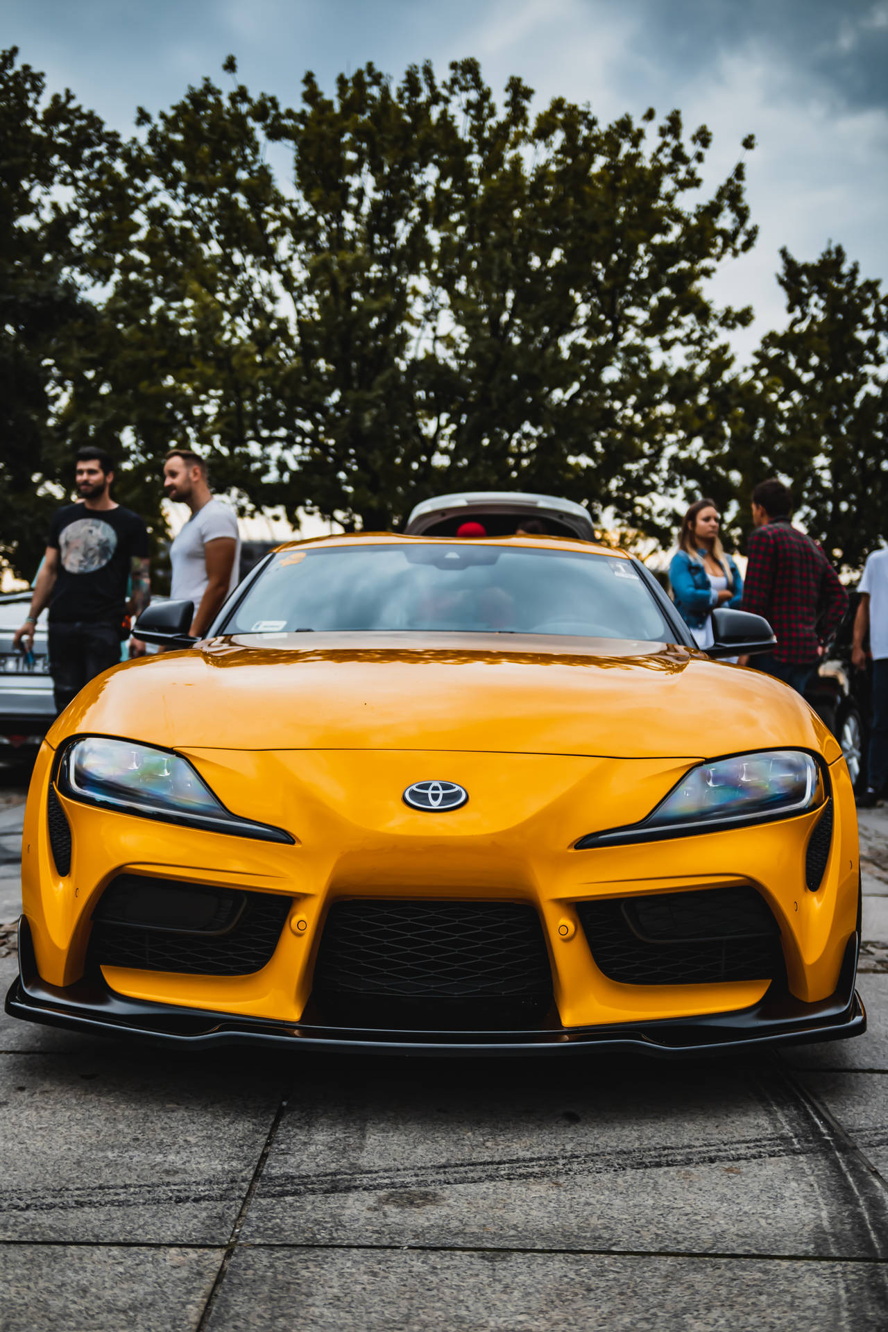 黃色豐田Supra跑車，附近有站在鋪砌停車場上的人們。 — Toyota Supra 壁紙