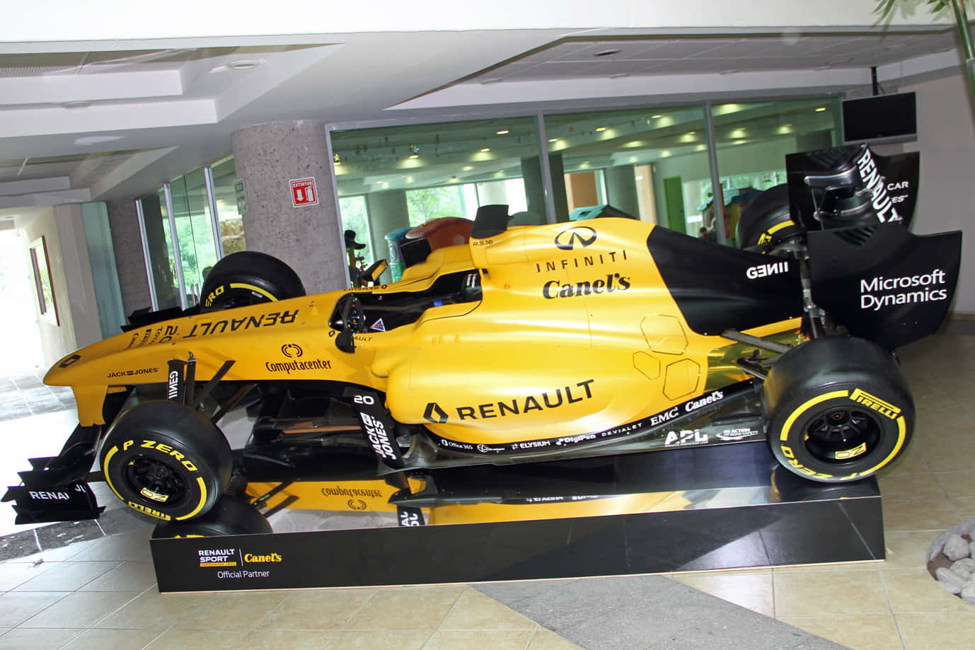 Renault Rs16 桌布 壁紙 — 一輛鮮黃色的雷諾一級方程式賽車，帶有黑色點綴和贊助商標誌，展示在現代室內大廳的基座上。